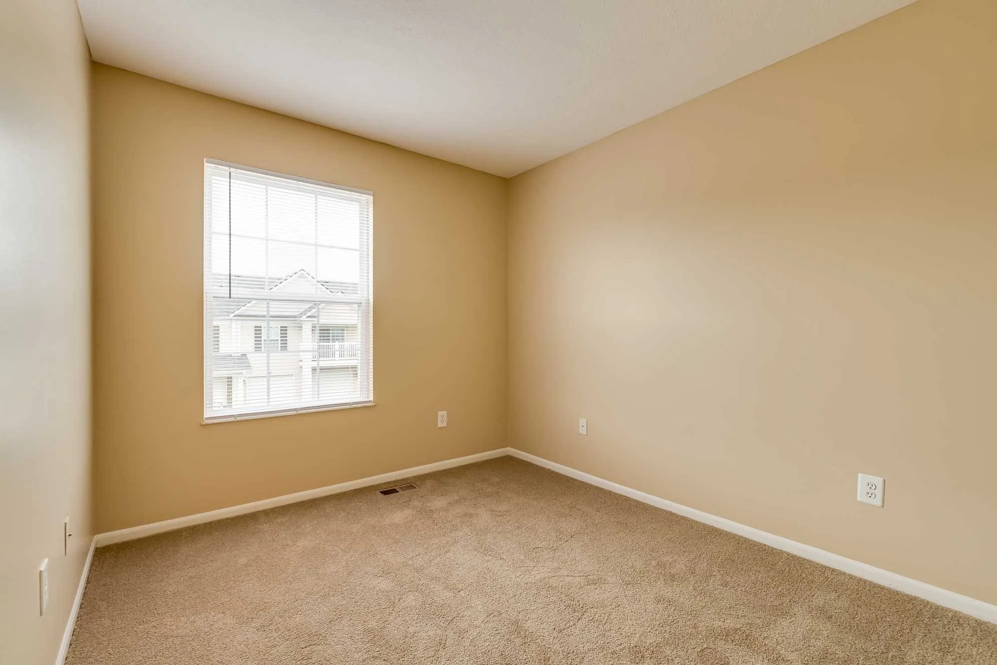 Empty room with beige walls, a window with blinds, beige carpet, and multiple electrical outlets.