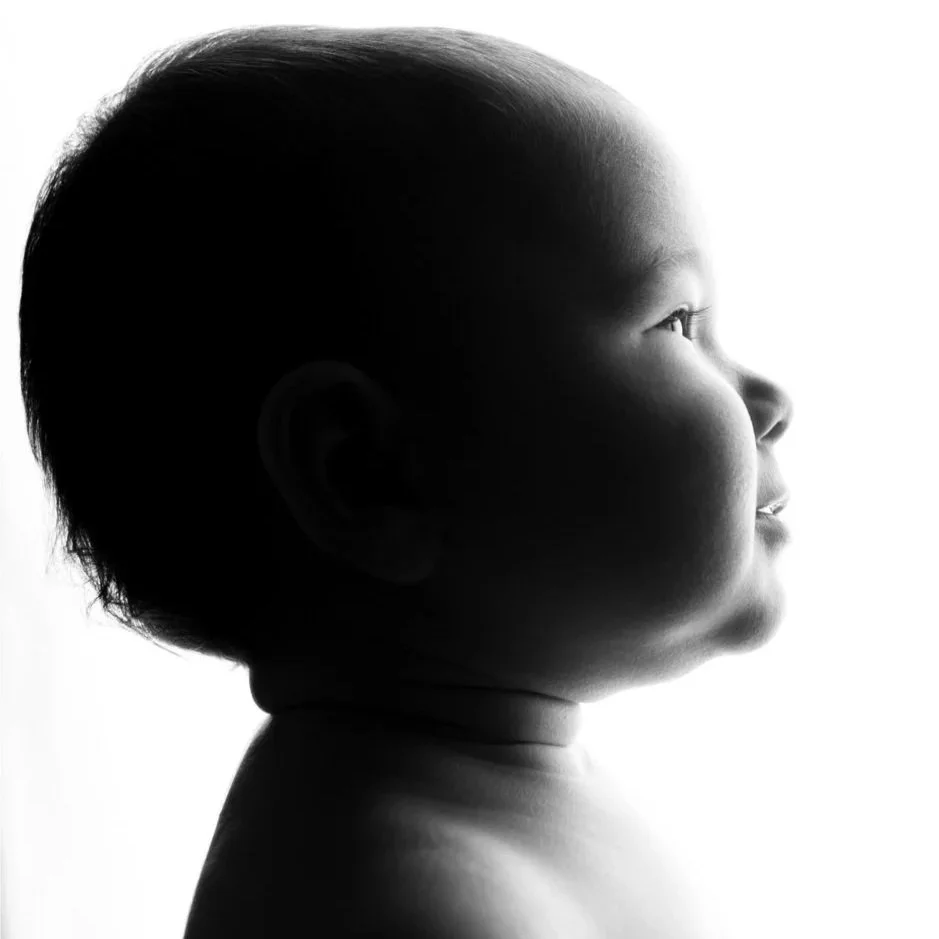 Profilo di un bambino neonatale in bianco e nero, con luce dietro, che guarda verso destra.