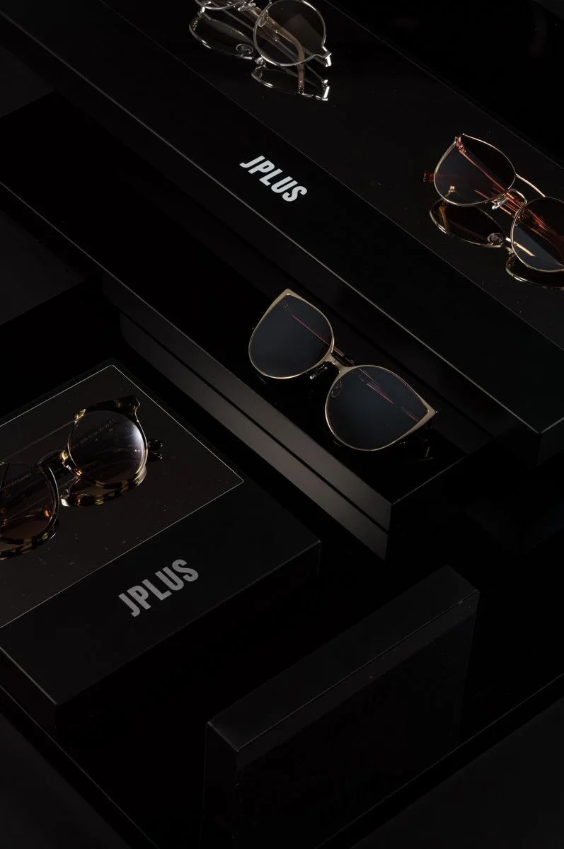 Occhiali da sole di moda esposti su scatole nere con il logo 'JPLus'.