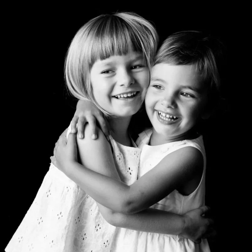 Due bambine che si abbracciano sorridenti in bianco e nero.