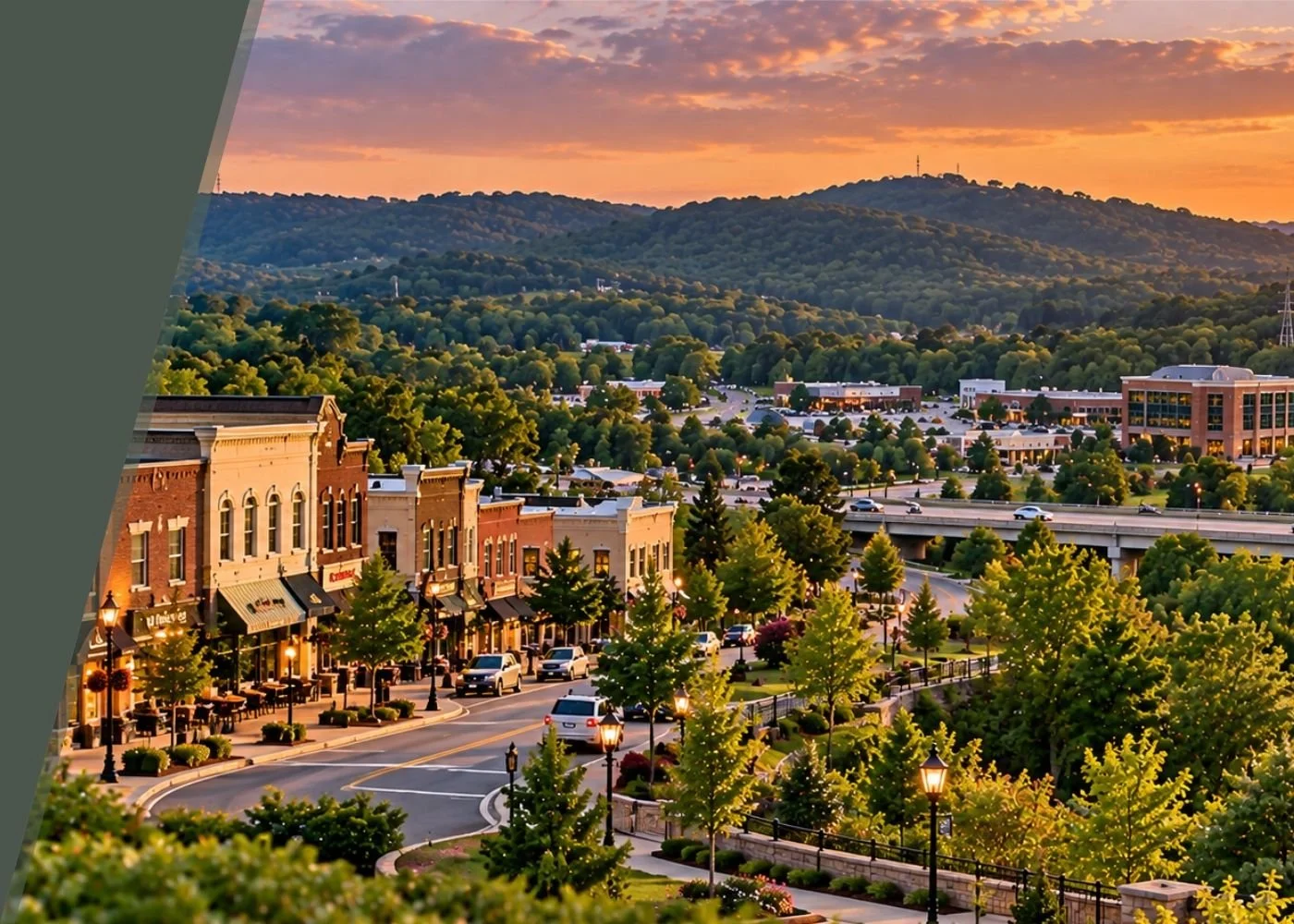 Downtown shopping area at sunset with colorful sky, lined with trees, street lamps, storefronts, and cars, with a mountain range in the background.