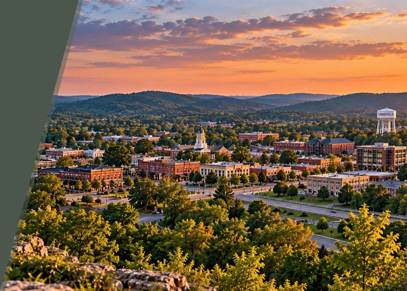 Overview of a small town at sunset with hills in the distance, featuring brick buildings, a clock tower, and a water tower labeled 'Cookeville,' surrounded by green trees and roads.