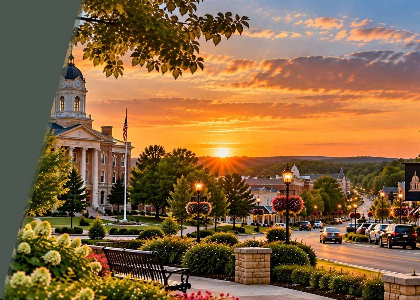 A small town at sunset with a historic courthouse, colorful flowers, trees, street lamps, and cars on a curved road.
