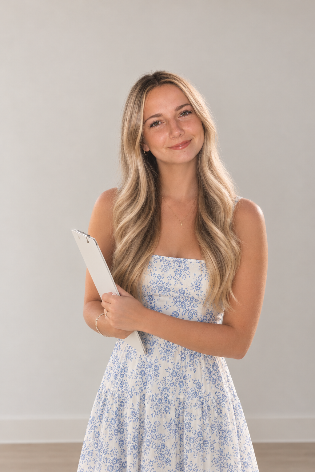 Smiling young woman with long blonde hair holding a clipboard and wearing a blue-and-white floral dress