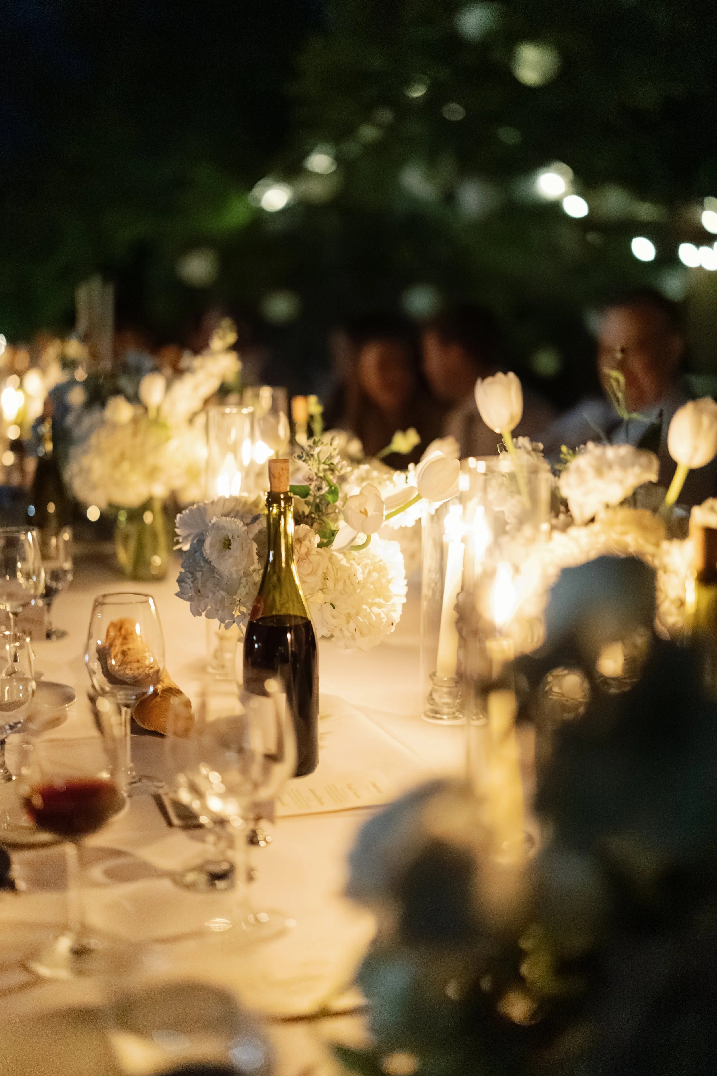 Elegant candlelit dinner table with white flowers, wine, glassware, and warm string lights