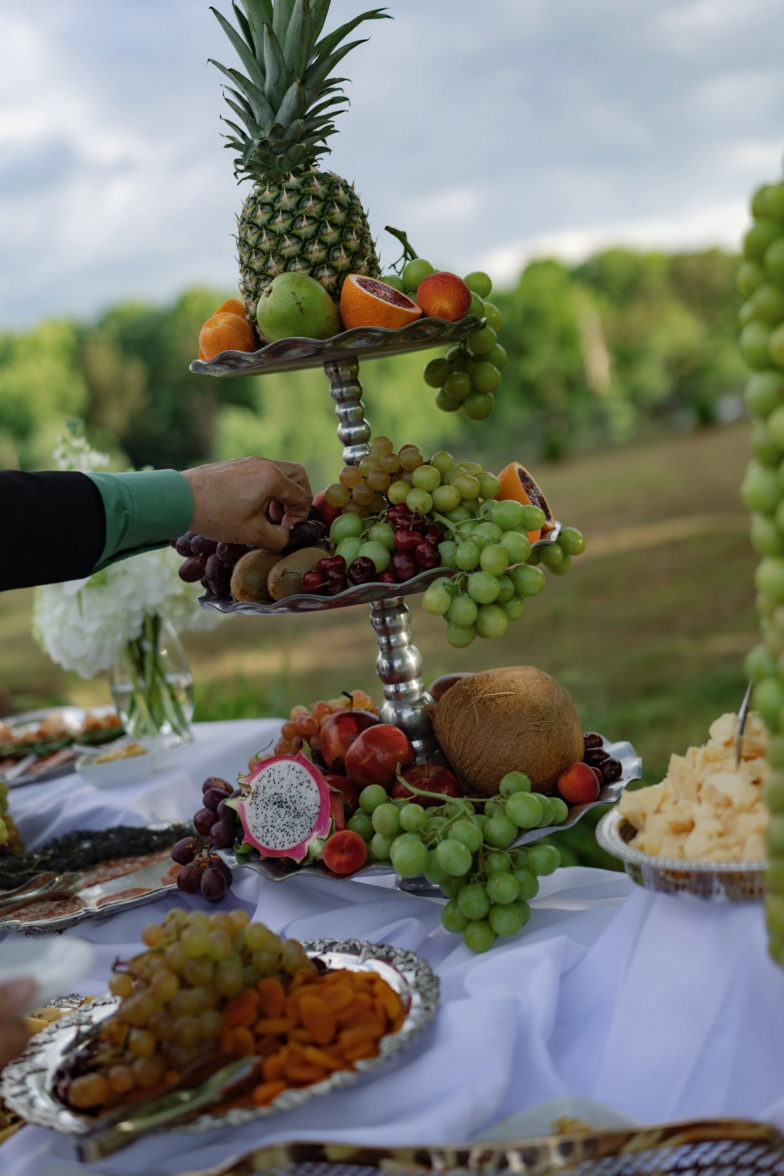 Celebration fruit display with pineapple, oranges, grapes, apples, kiwi, dragon fruit, and coconut on ornate serving stands