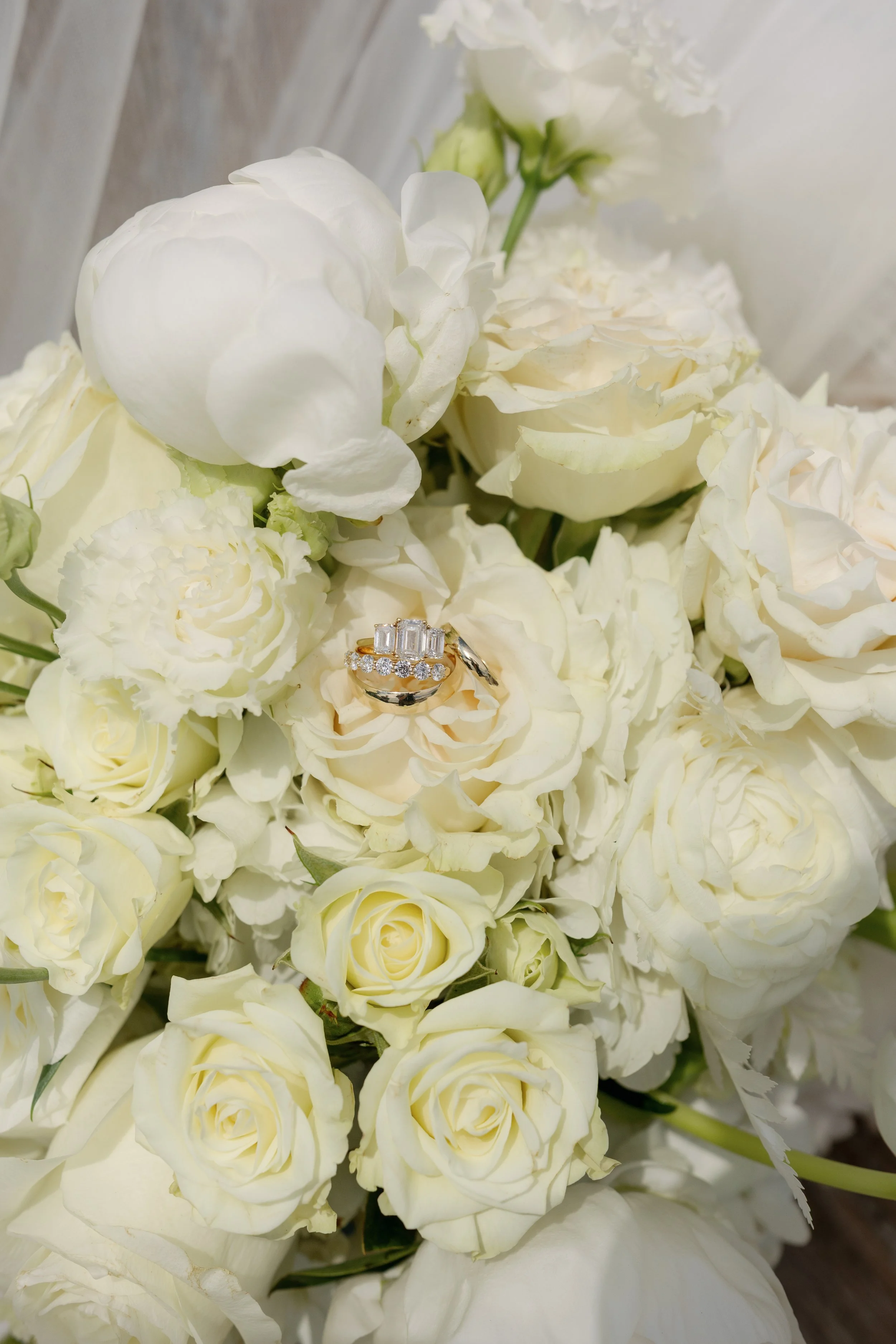 Close-up of white roses and other flowers surrounding a diamond wedding ring