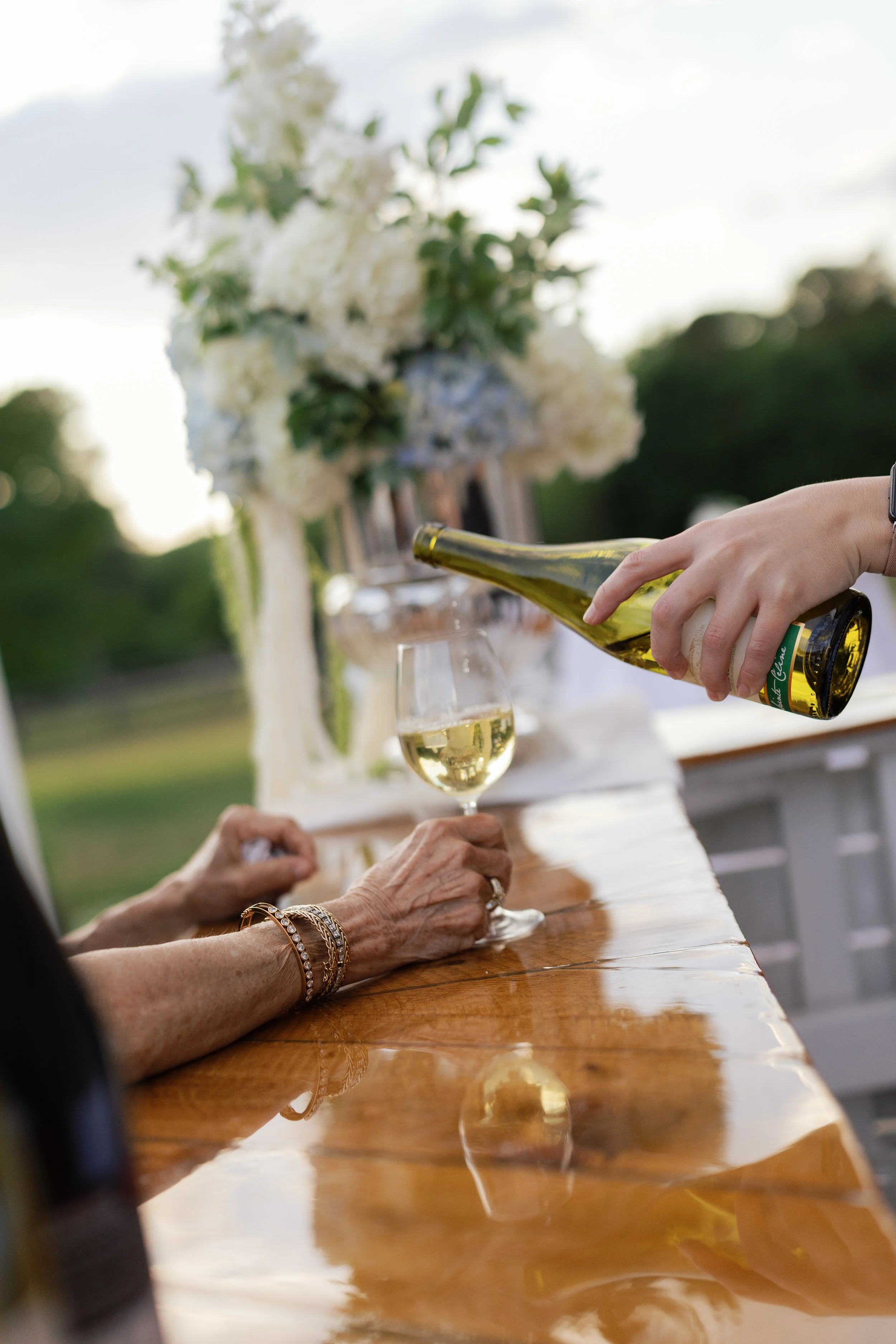 Person pouring white wine into a glass at a table decorated with white flowers.