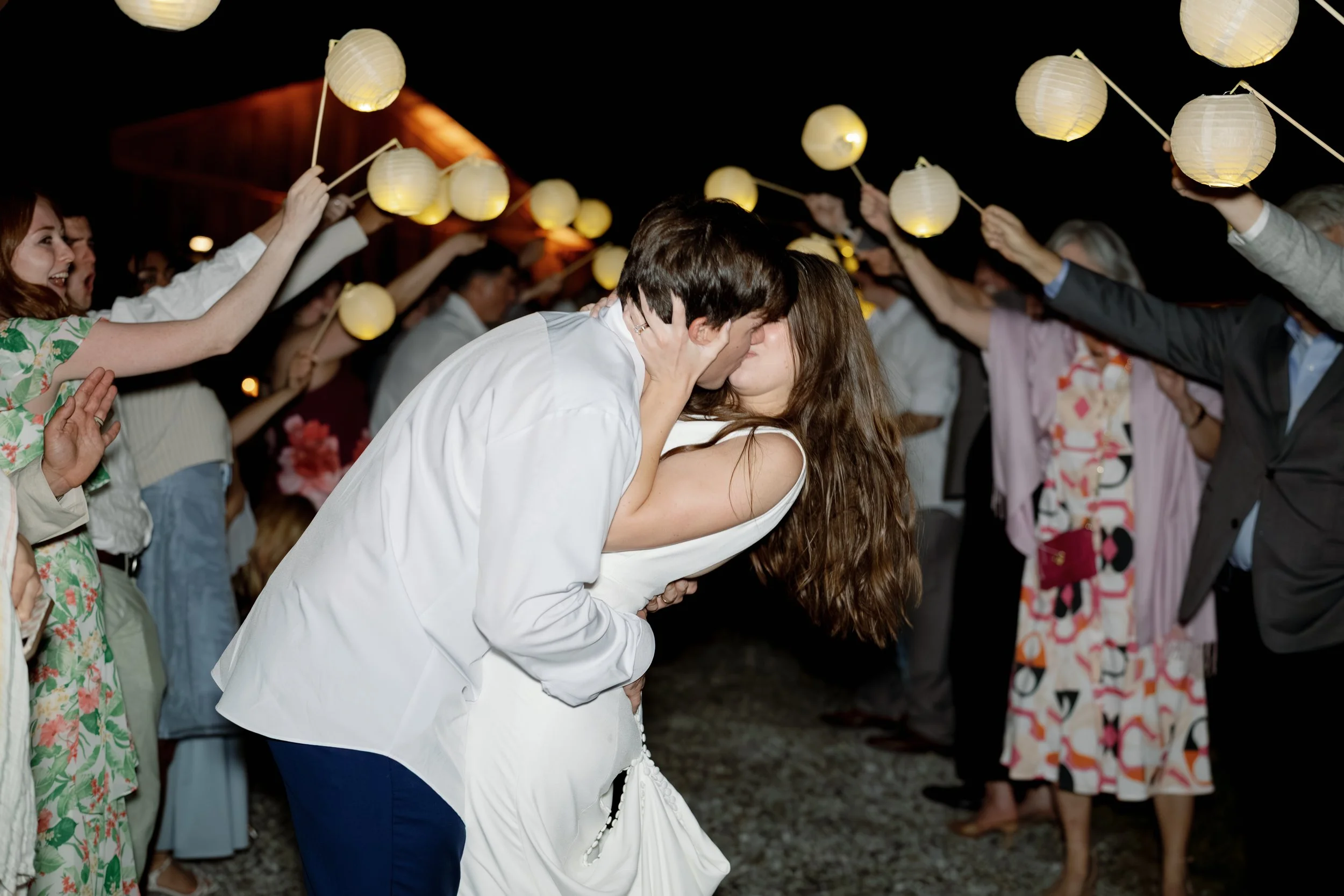 Newlywed couple kissing and dancing at a wedding reception surrounded by guests holding glowing paper lanterns