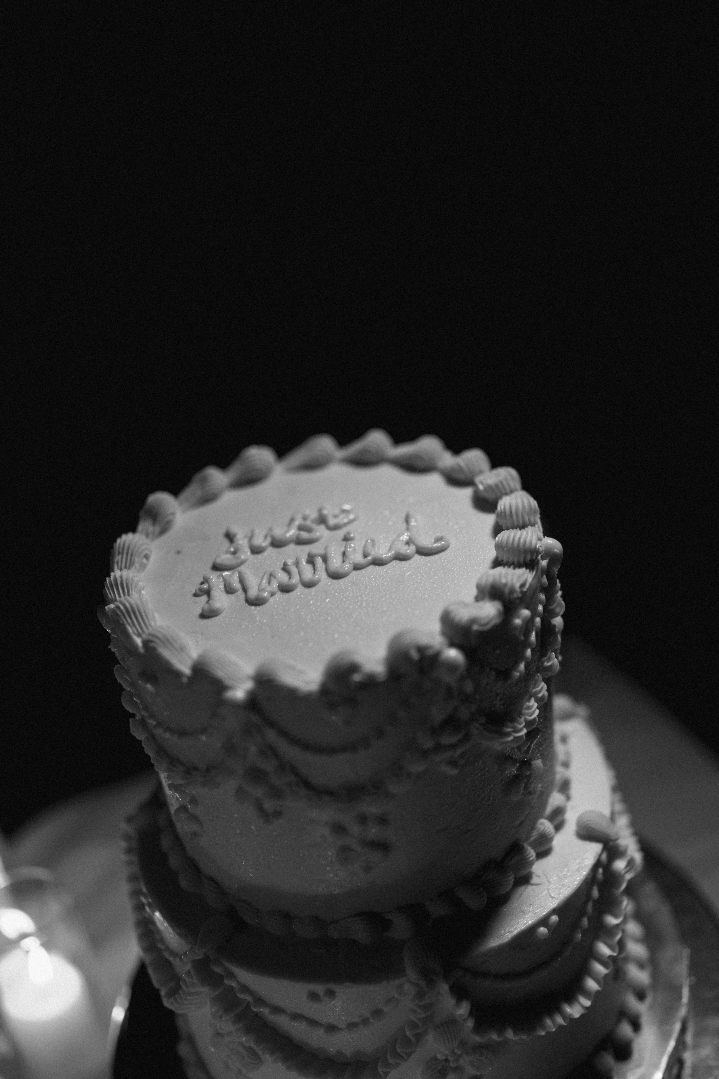 Close-up black-and-white photo of a decorated birthday cake with piped frosting borders and cursive writing on top