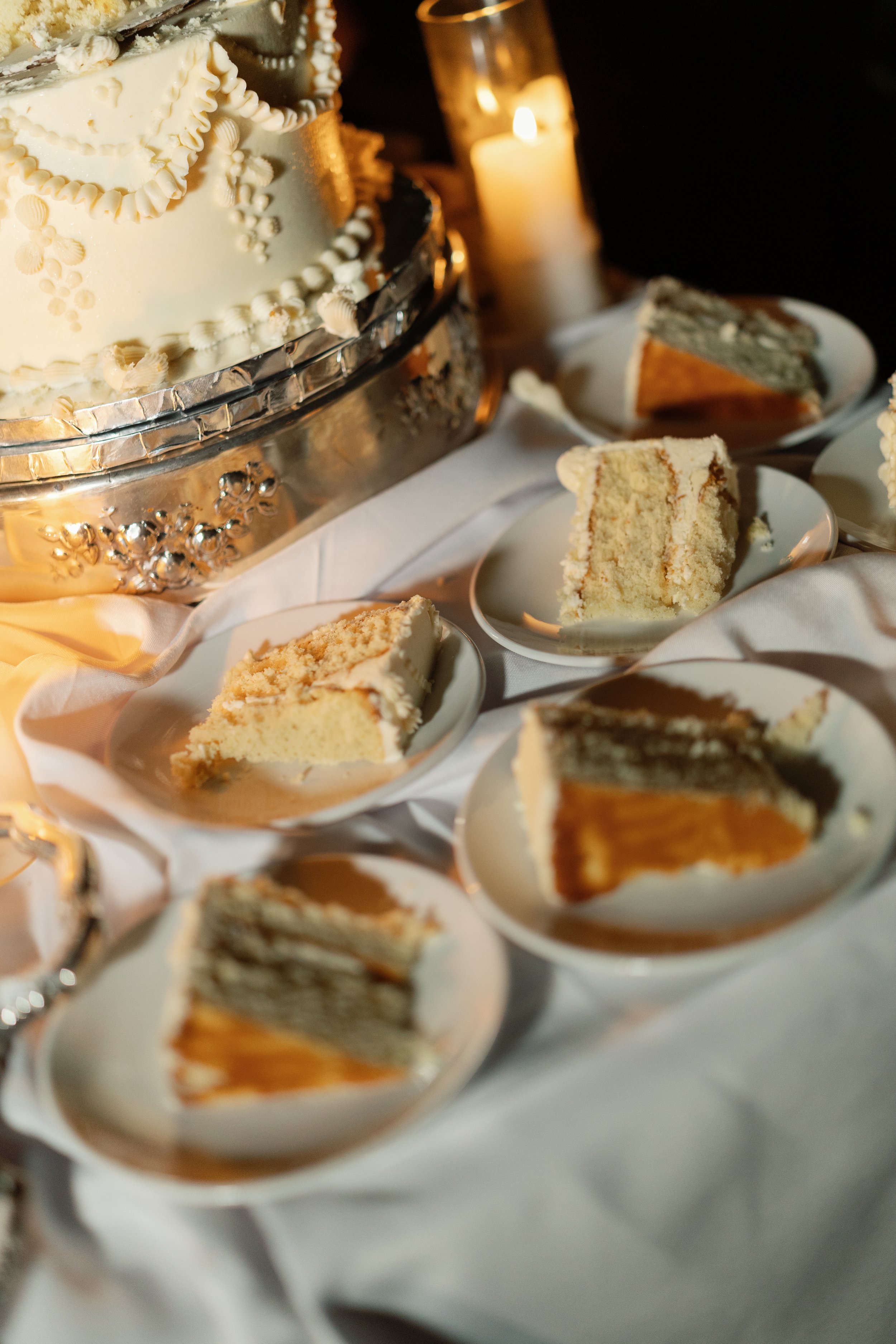Decorated white wedding cake with sliced cake on plates and a glowing candle at a reception table