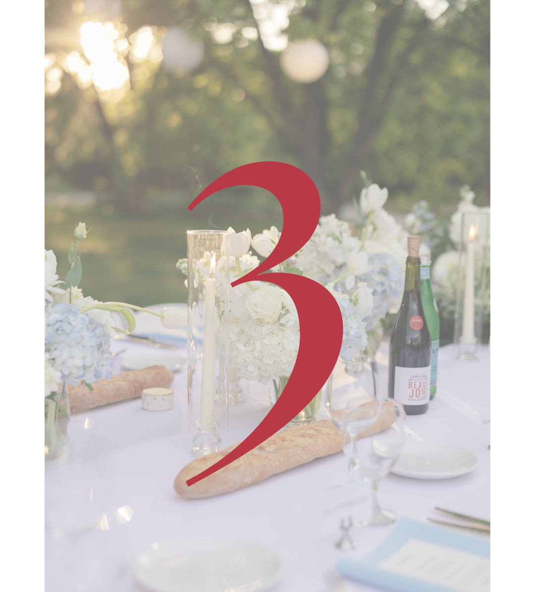 Elegant outdoor wedding table with white flowers, candles, baguettes, wine bottles, and a large red number 3