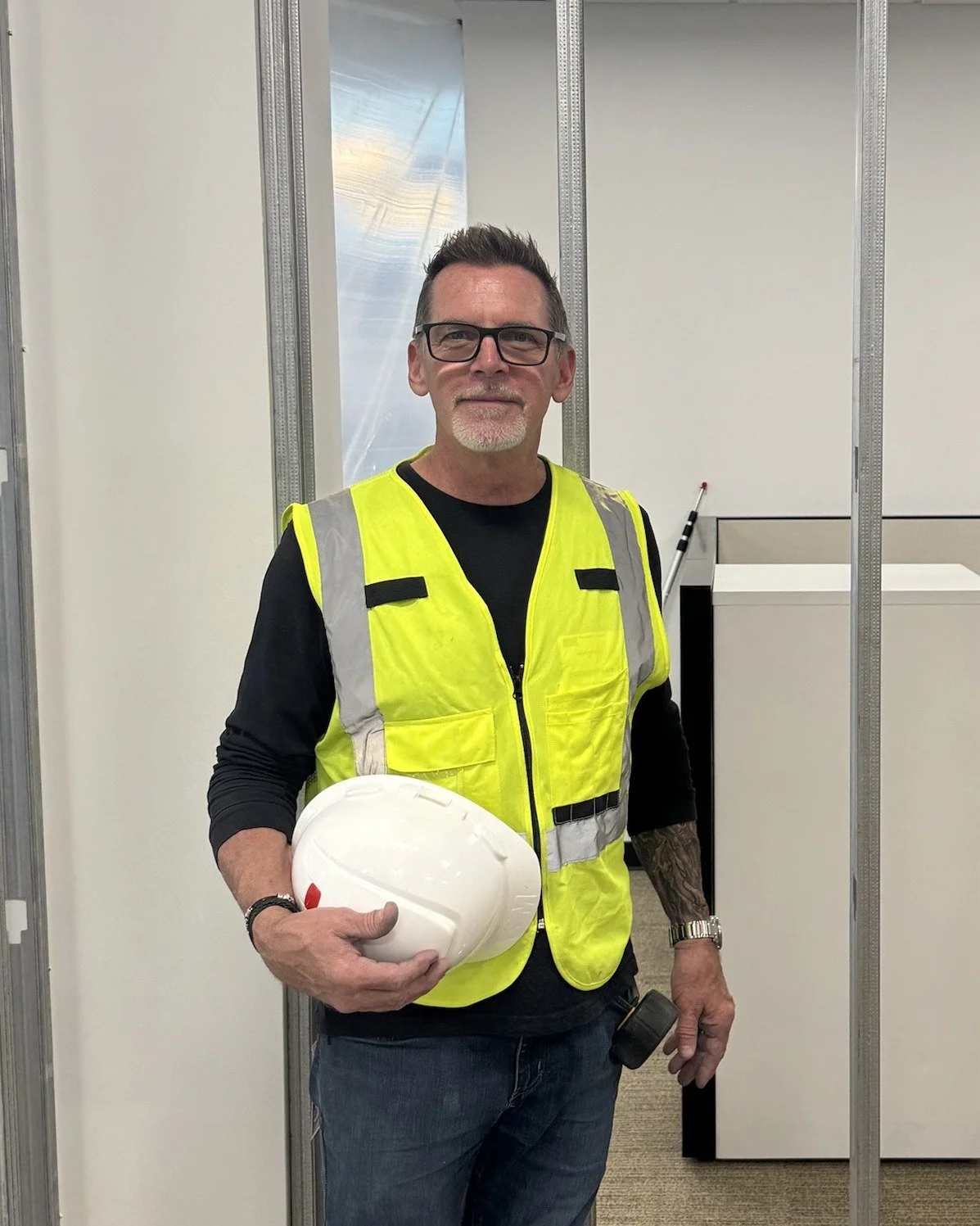 Man in safety vest holding white hardhat inside a construction site or office under construction