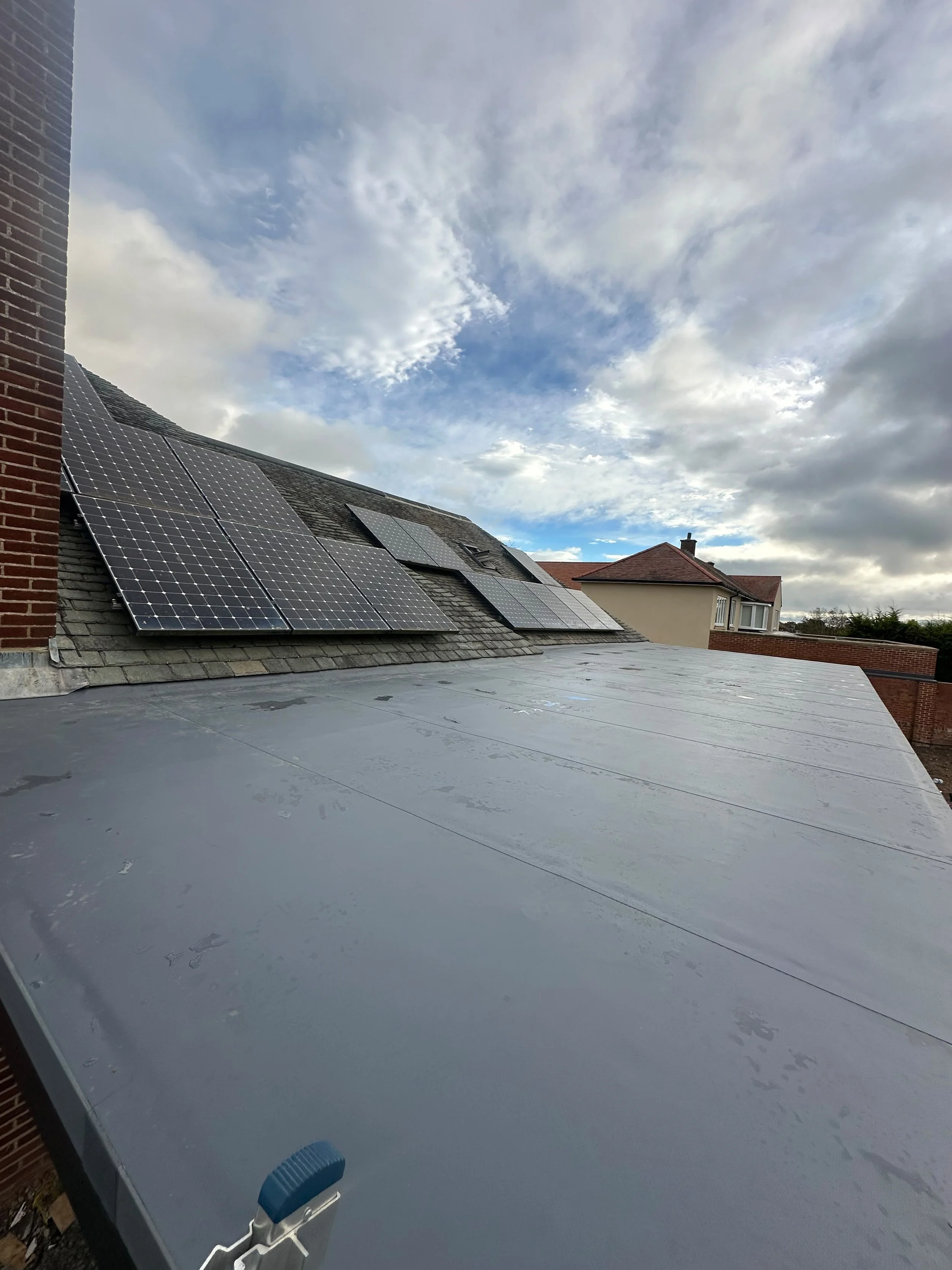 View of a rooftop with solar panels installed on the sloped roof, under a partly cloudy sky.