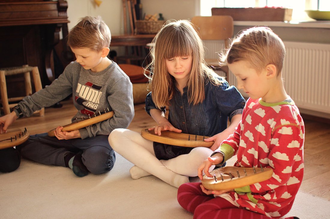 Three children sitting on the floor playing a musical instrument called a kalimba in a cozy room.