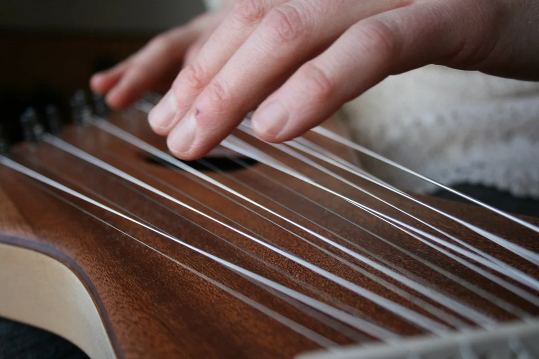 Close-up of a person's hand plucking the strings of an acoustic guitar with a wooden body.