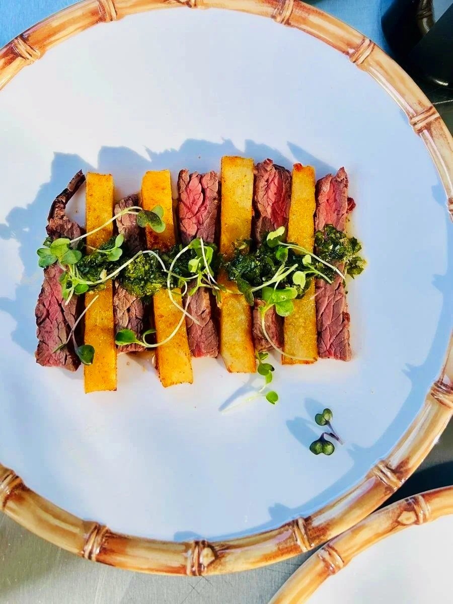Sliced medium-rare steak with crispy golden fries and microgreens on a white plate with a bamboo rim.