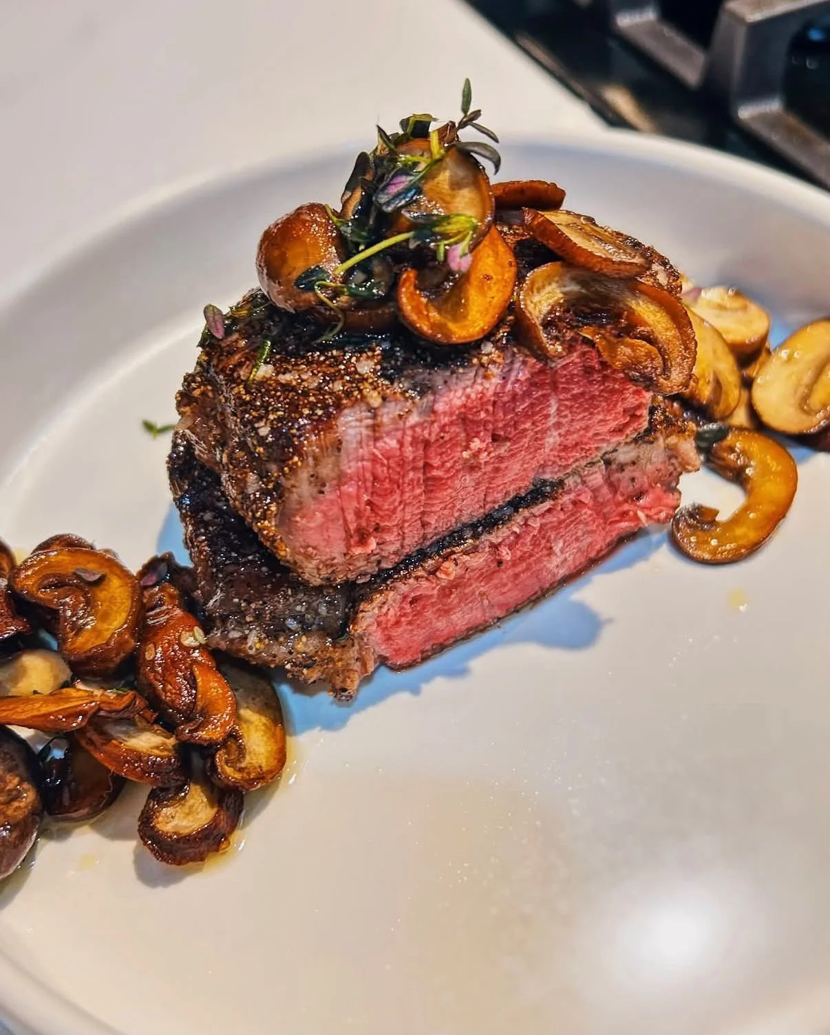 A plate of medium-rare cooked steak topped with sautéed mushrooms.