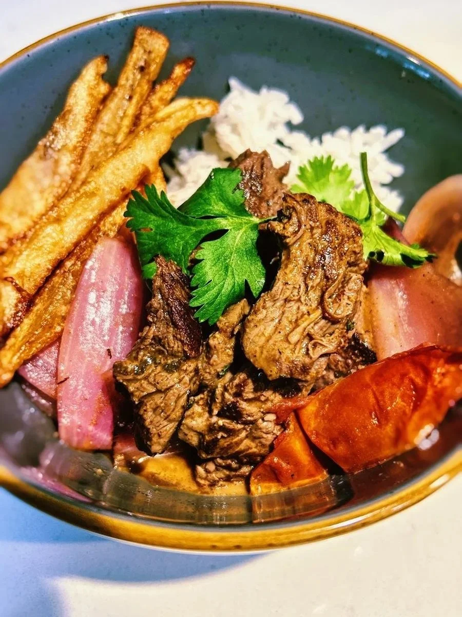 A bowl with fried potato fries, sliced ham, beef brisket, lobster tail, white rice, and garnished with cilantro.