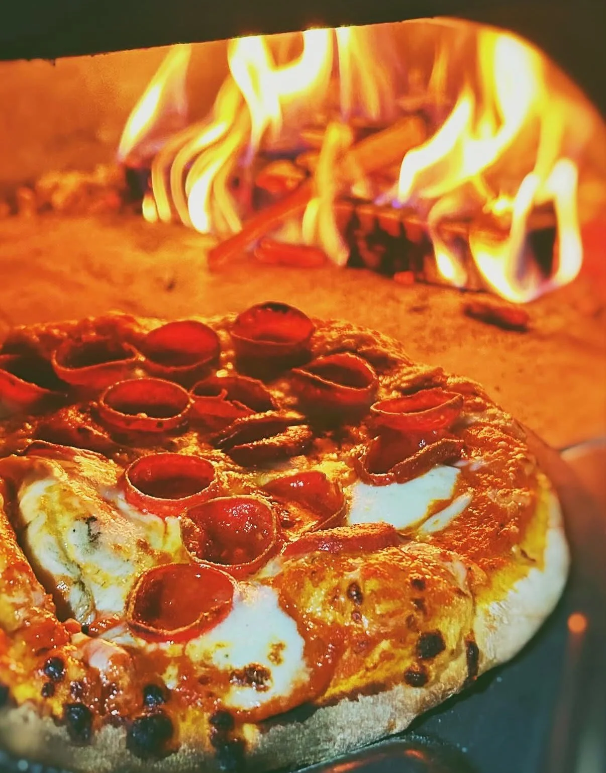 Pepperoni pizza baking in an oven with flames visible in the background.
