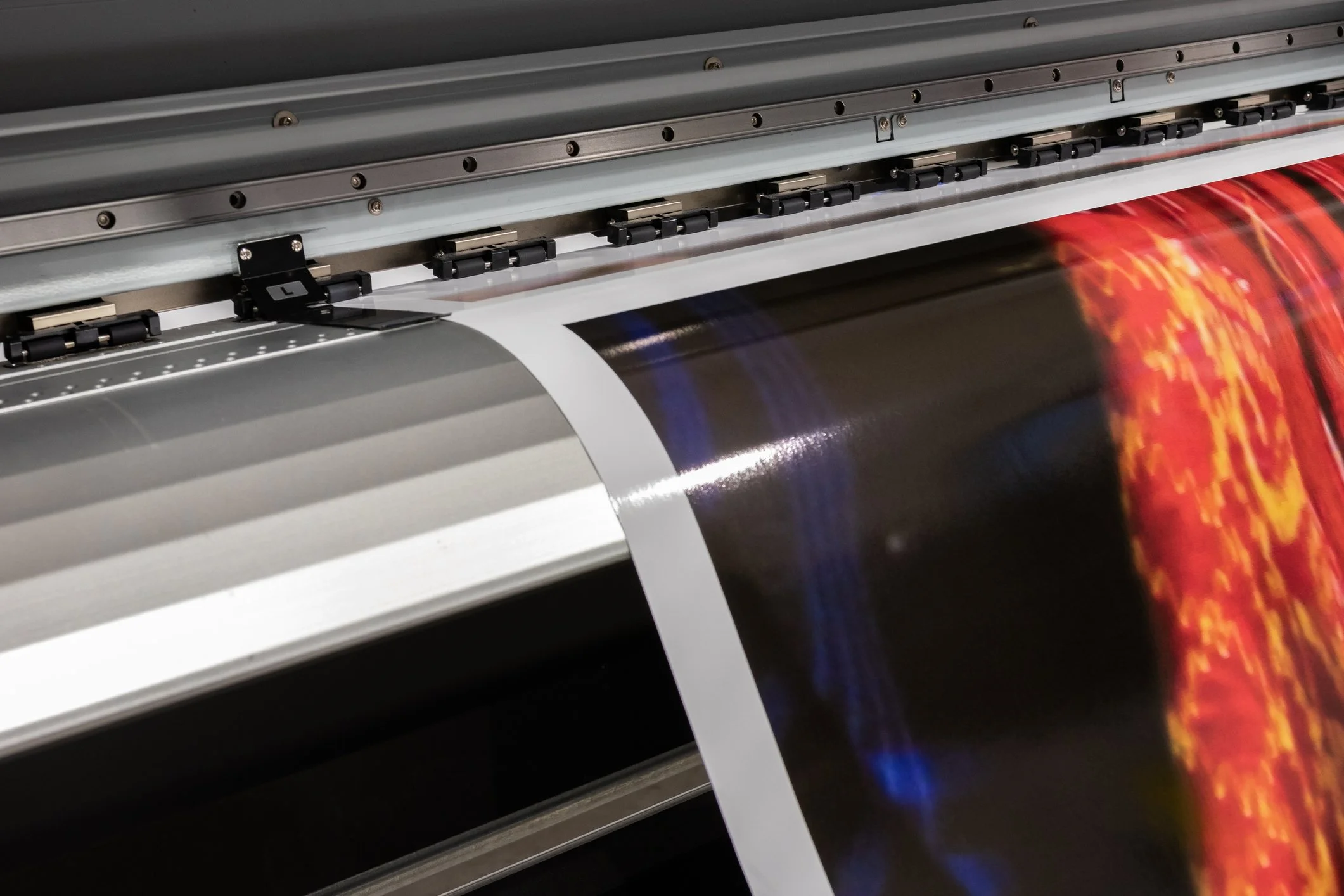 A large format printer printing a colorful image, possibly a digital or poster print, with paper guided through rollers.