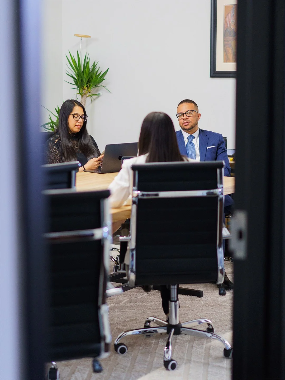 The Castro Injury Team in a business meeting in a modern office, seated around a wooden conference table, with one woman seen from the back and two others facing her.