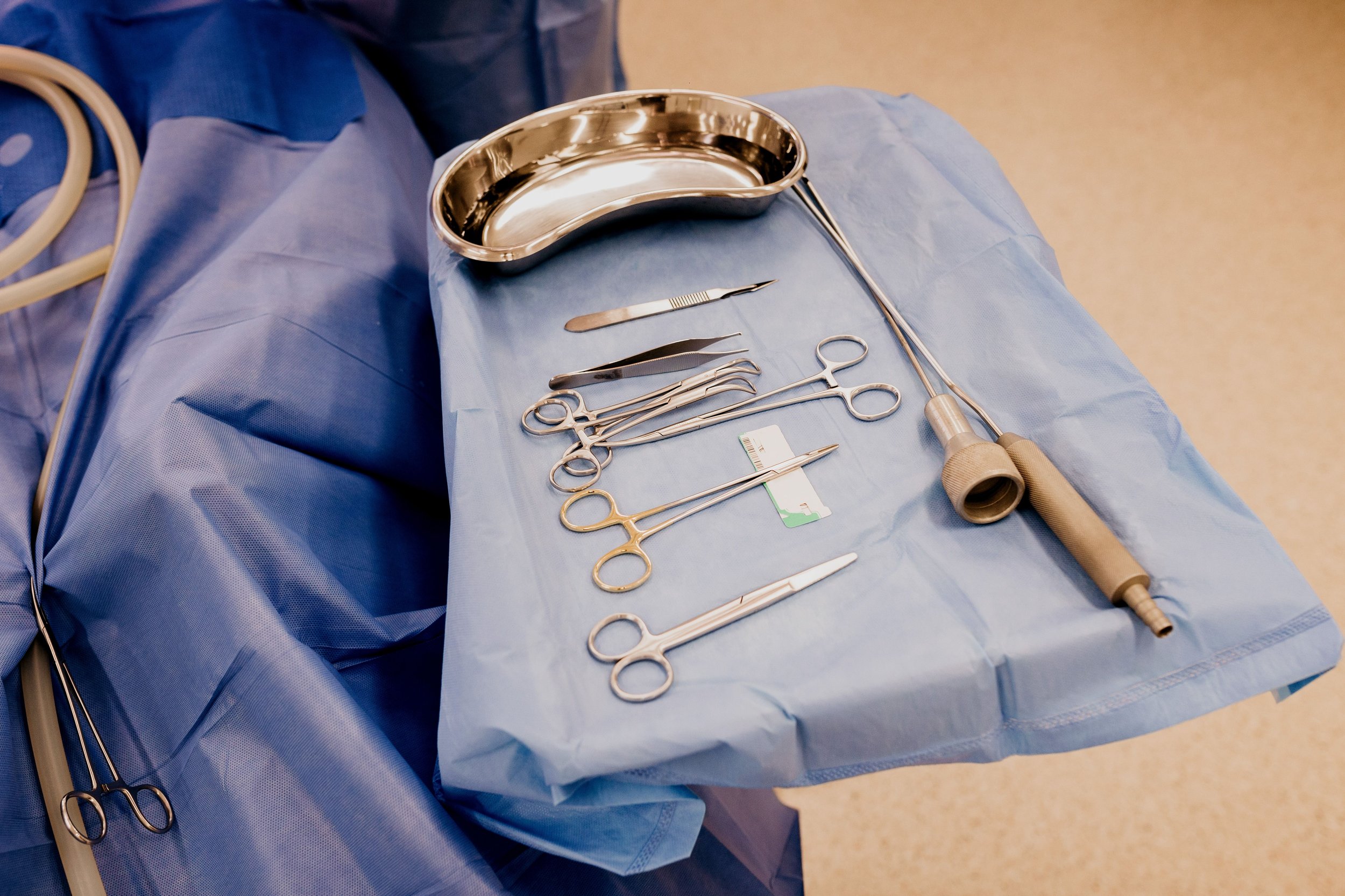 A surgical setup with various surgical instruments arranged on a blue drape, including scissors, forceps, and a surgical lamp, in an operating room.