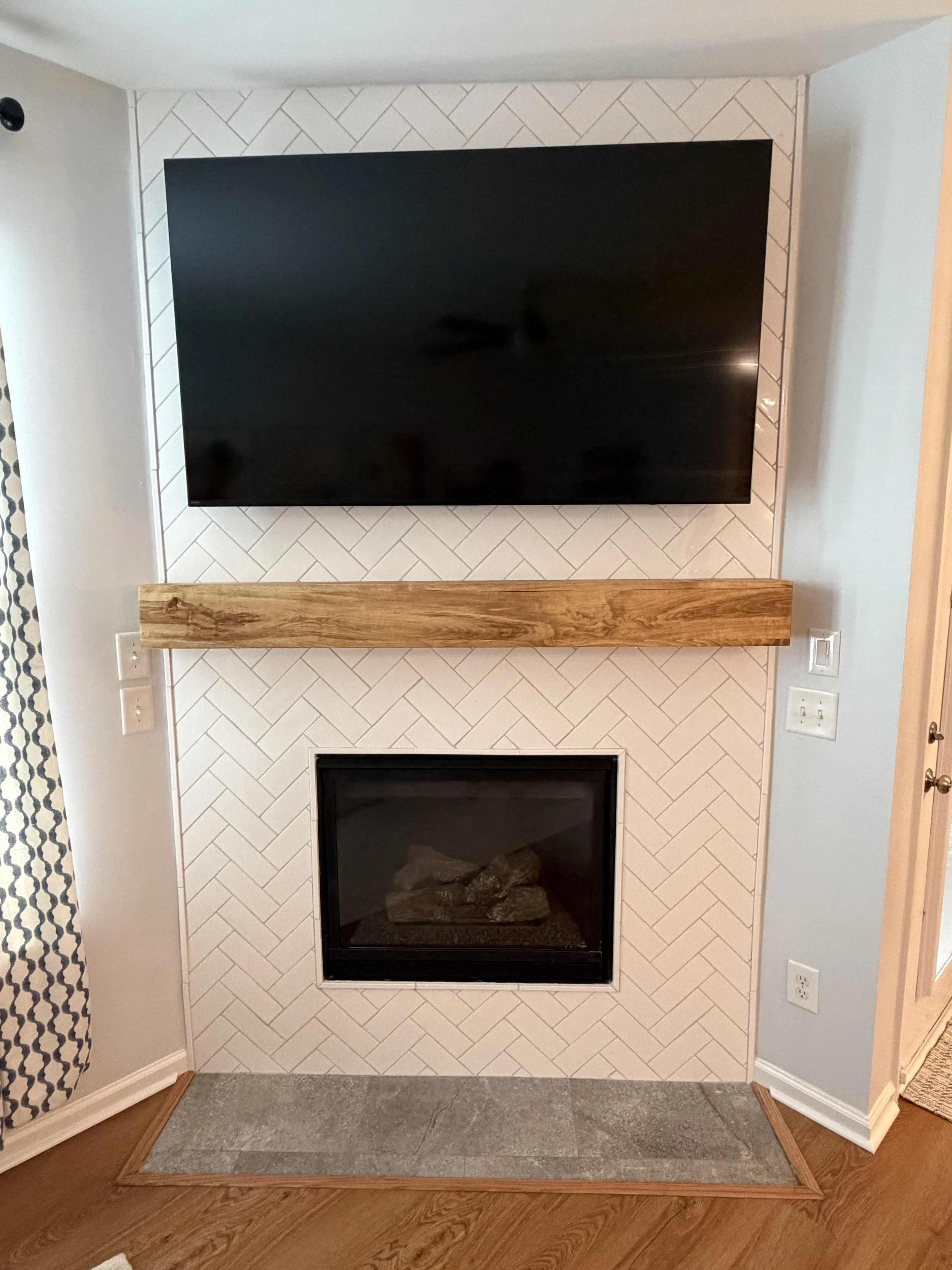 White herringbone tile and a warm wood mantel give this fireplace a fresh, inviting feel—a cozy focal point for quiet evenings and time together.