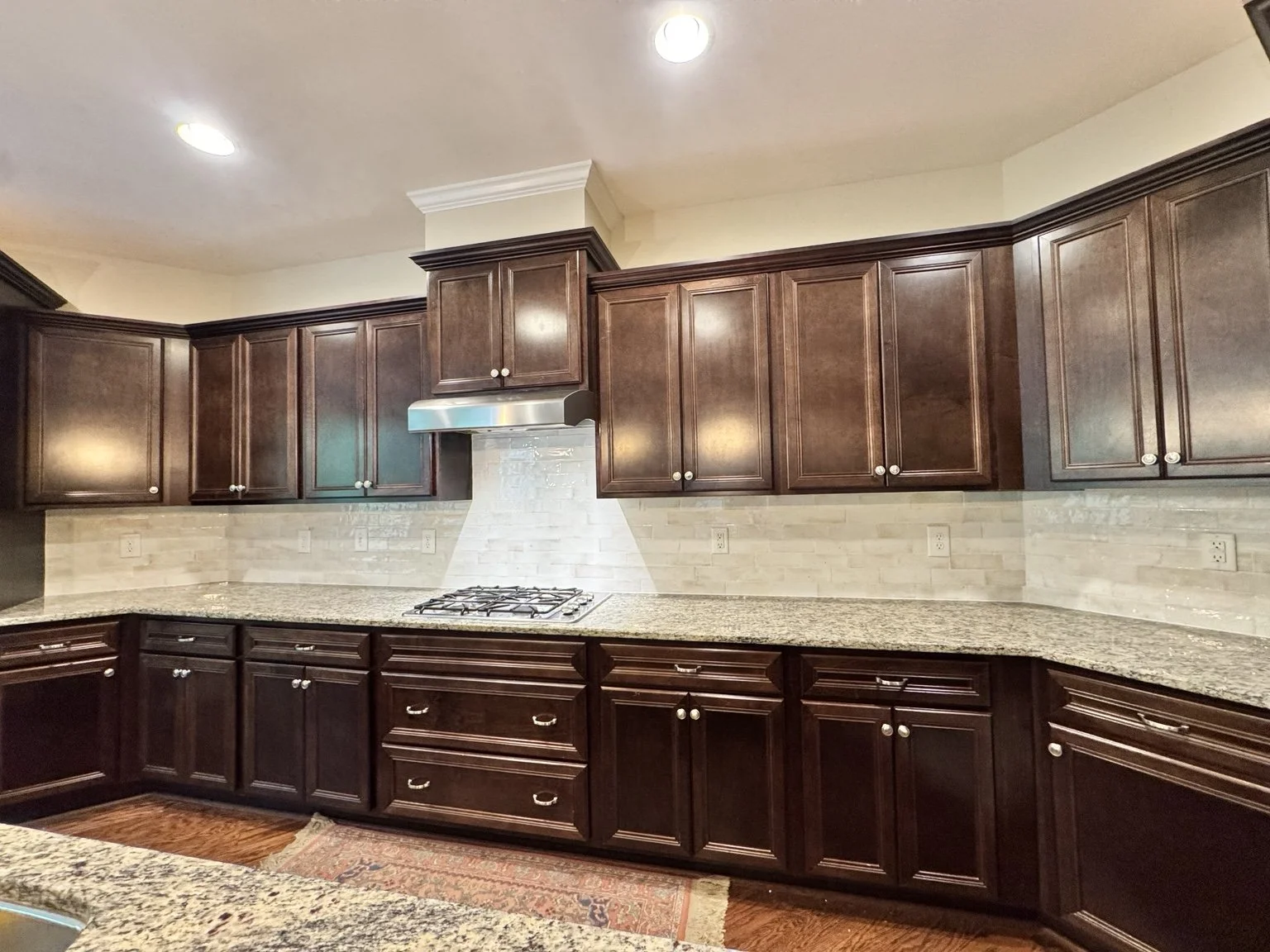 A patterned detail behind the cooktop adds a personal touch, while light backsplash tile balances the warmth of the wood cabinets.