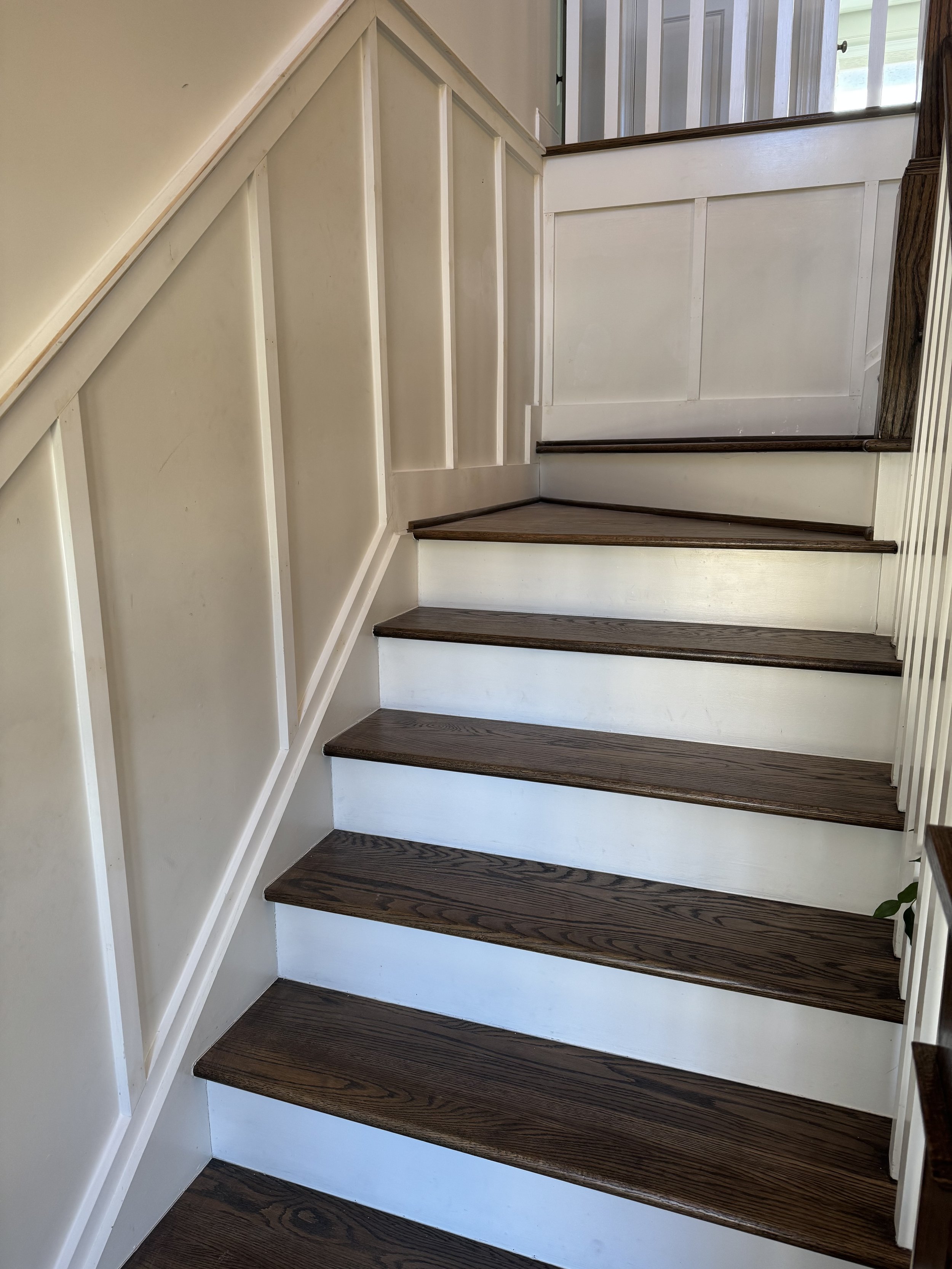 A staircase with dark-brown wooden steps and white risers, along with white steps and paneling on the side wall.