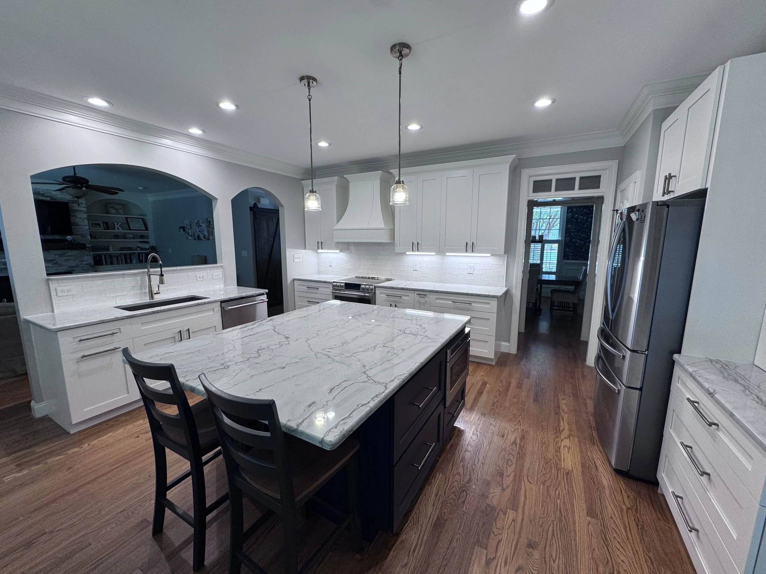 White kitchen cabinets with a dark island, light countertops, and pendant lights.