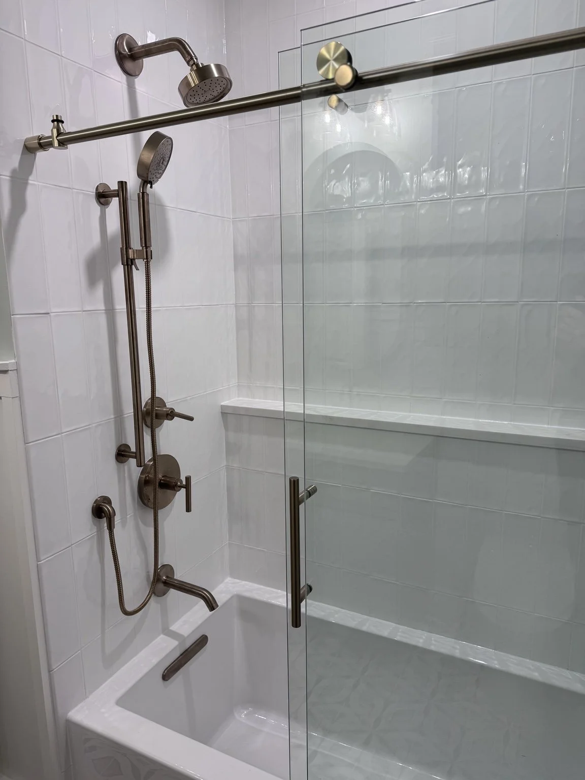 White tile and warm metal fixtures bring a soft, classic feel to this shower—a bright start to the morning and an easy place to refresh.