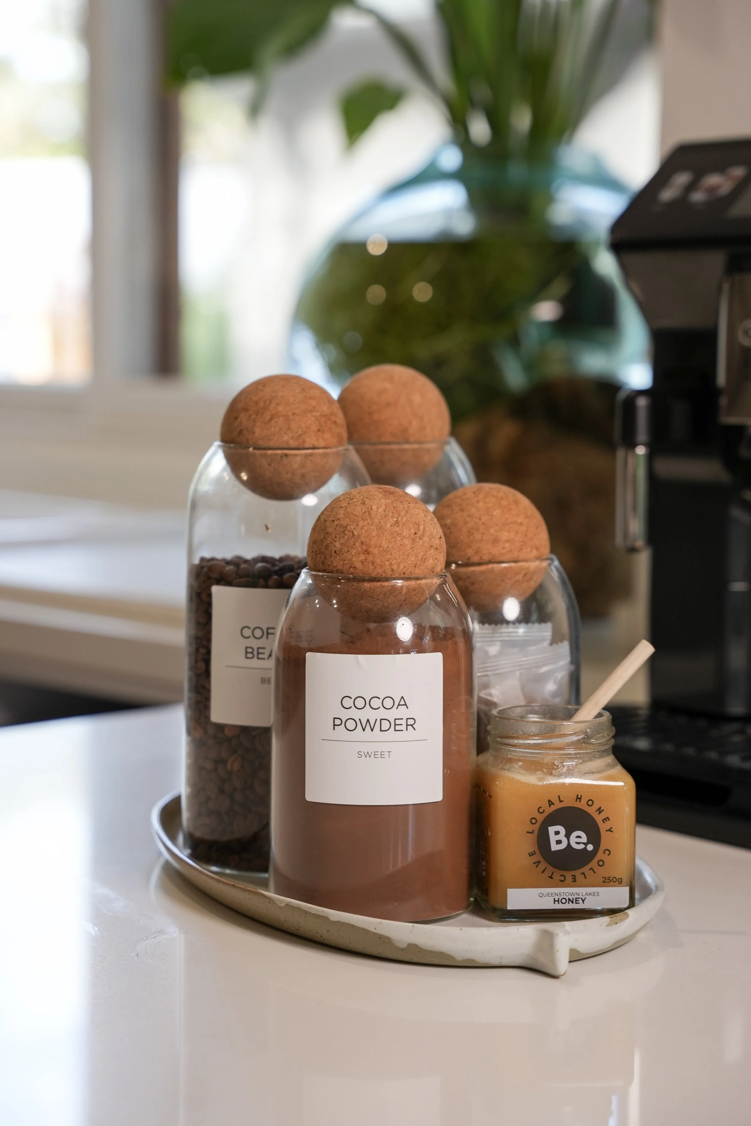 Coffee beans, cocoa powder, honey, and cookies on a white tray