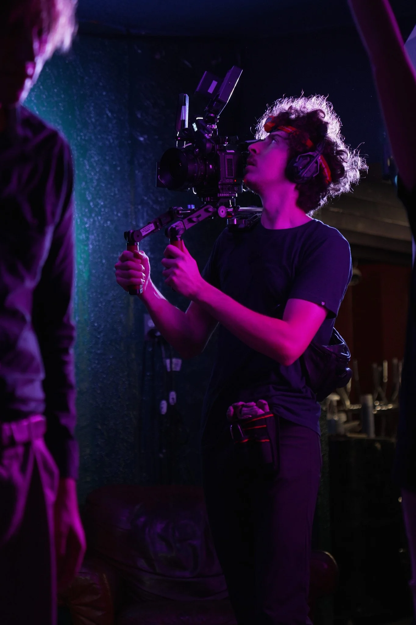 Filmmaker operating a professional camera rig under purple lighting on a film set