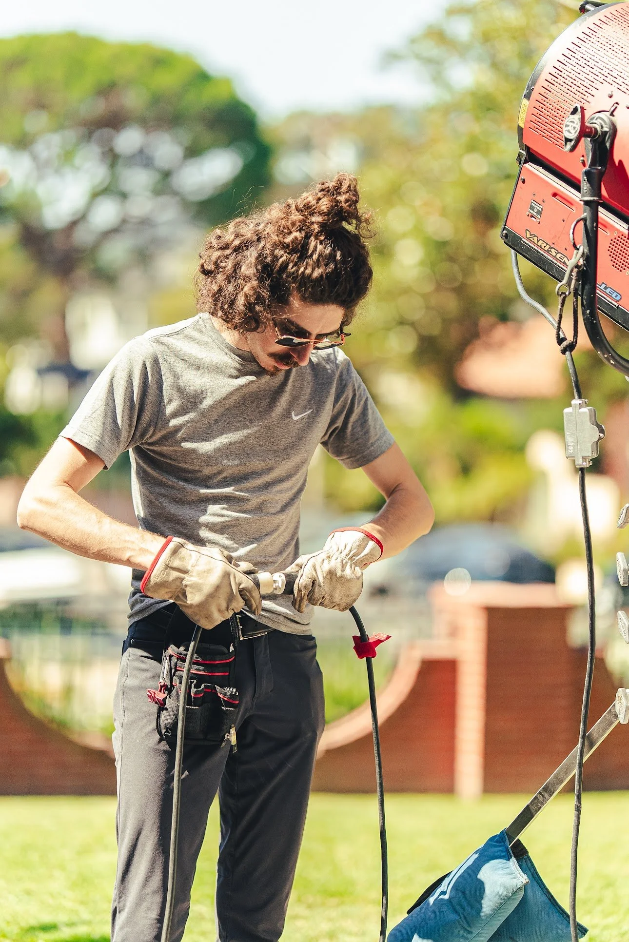 Outdoor technician wearing safety gloves and tool belt, operating equipment beside a large red machine.