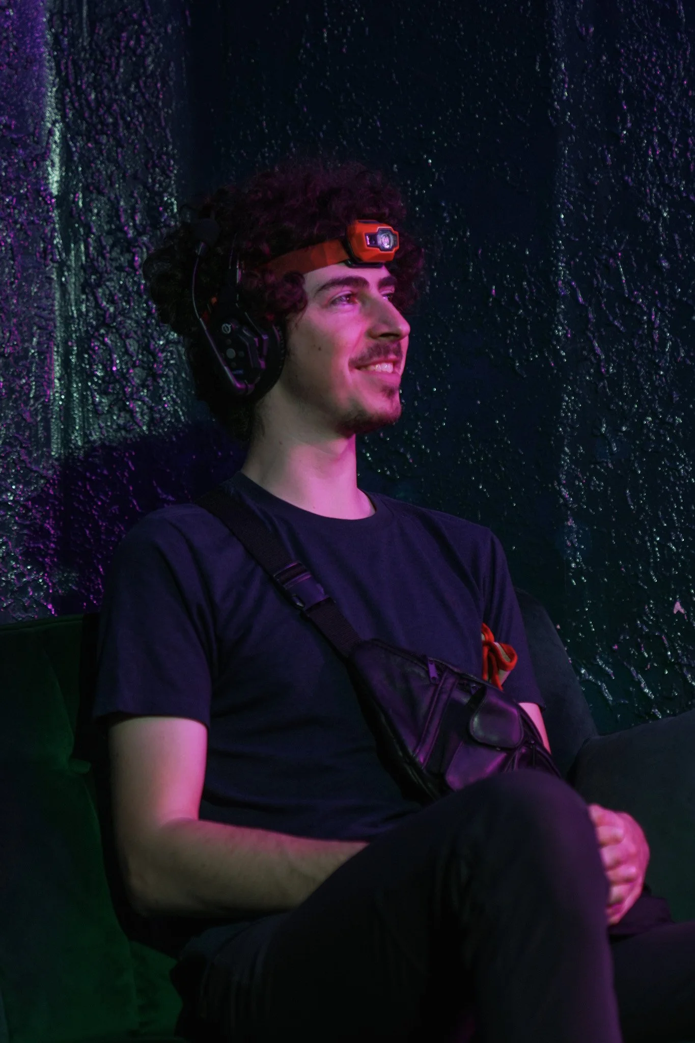 Young man wearing an orange headlamp and black headphones in purple lighting