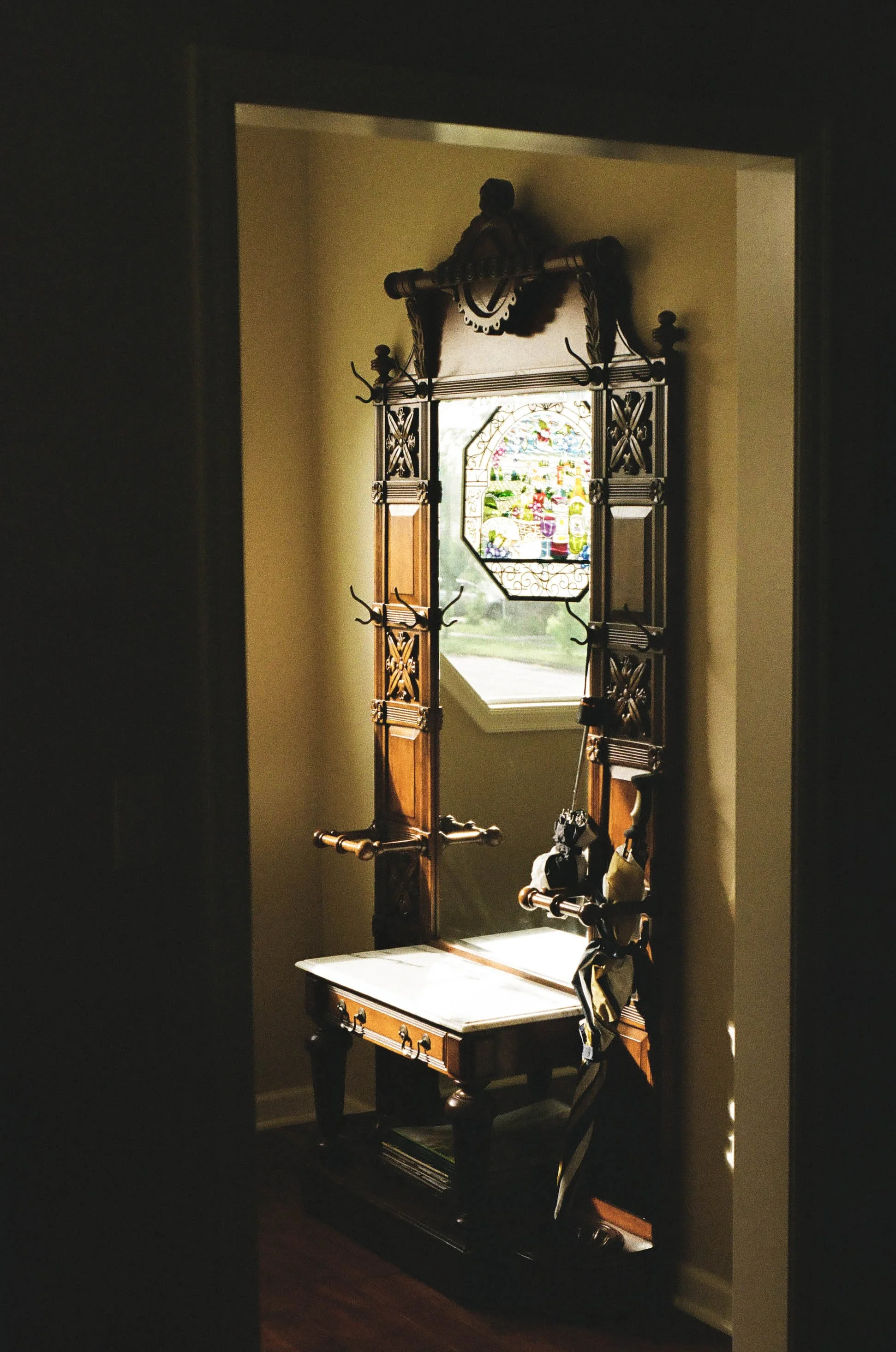 Ornate antique wooden hall tree with coat hooks, stained-glass mirror, and bench in a dimly lit entryway