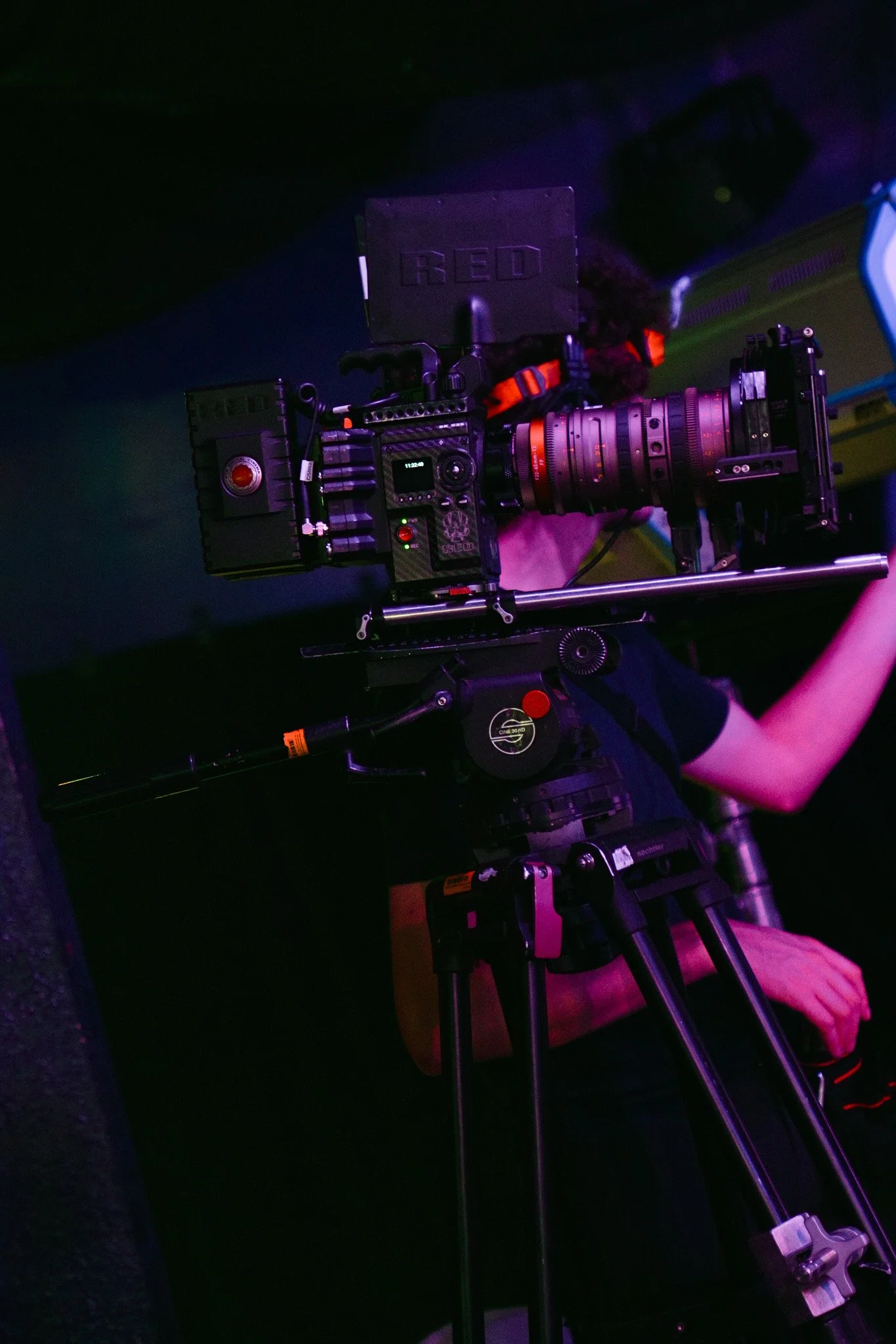 Professional RED cinema camera with telephoto lens mounted on a tripod in purple and blue lighting