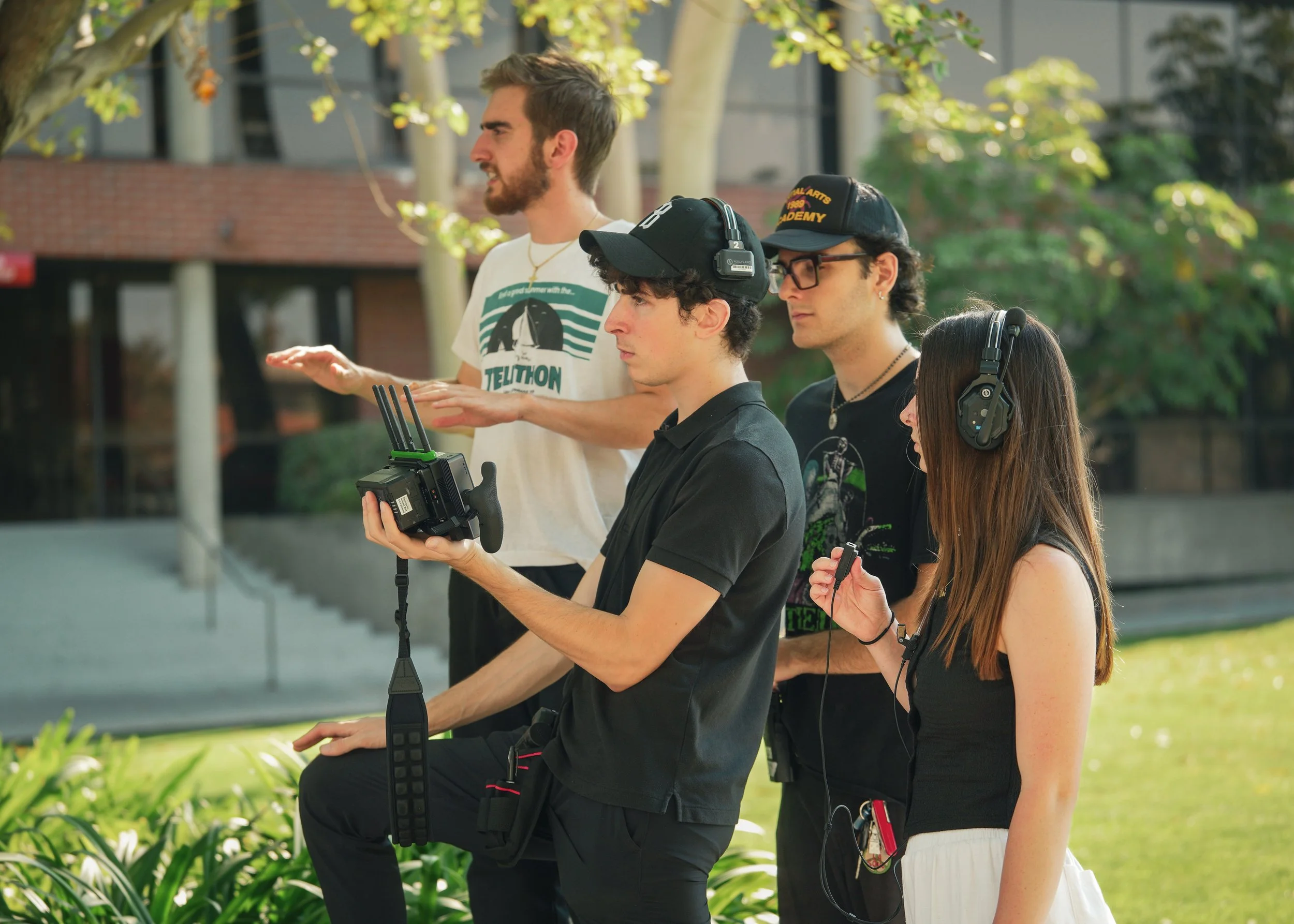 Film crew filming outdoors with a handheld camera, wireless audio equipment, and headphones.
