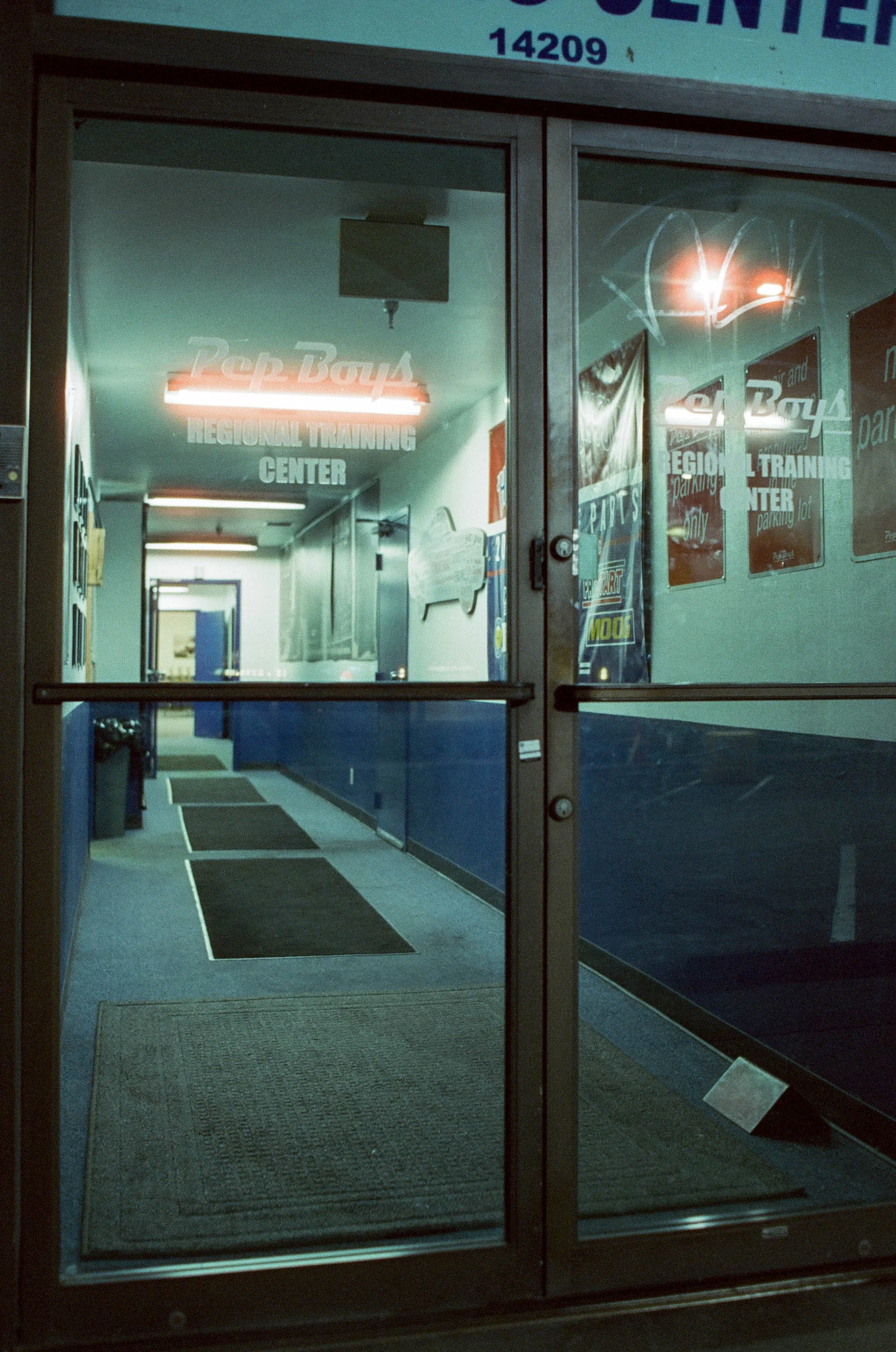 Glass entrance doors to a brightly lit airport terminal, with advertising posters and queue number 14209 visible above.