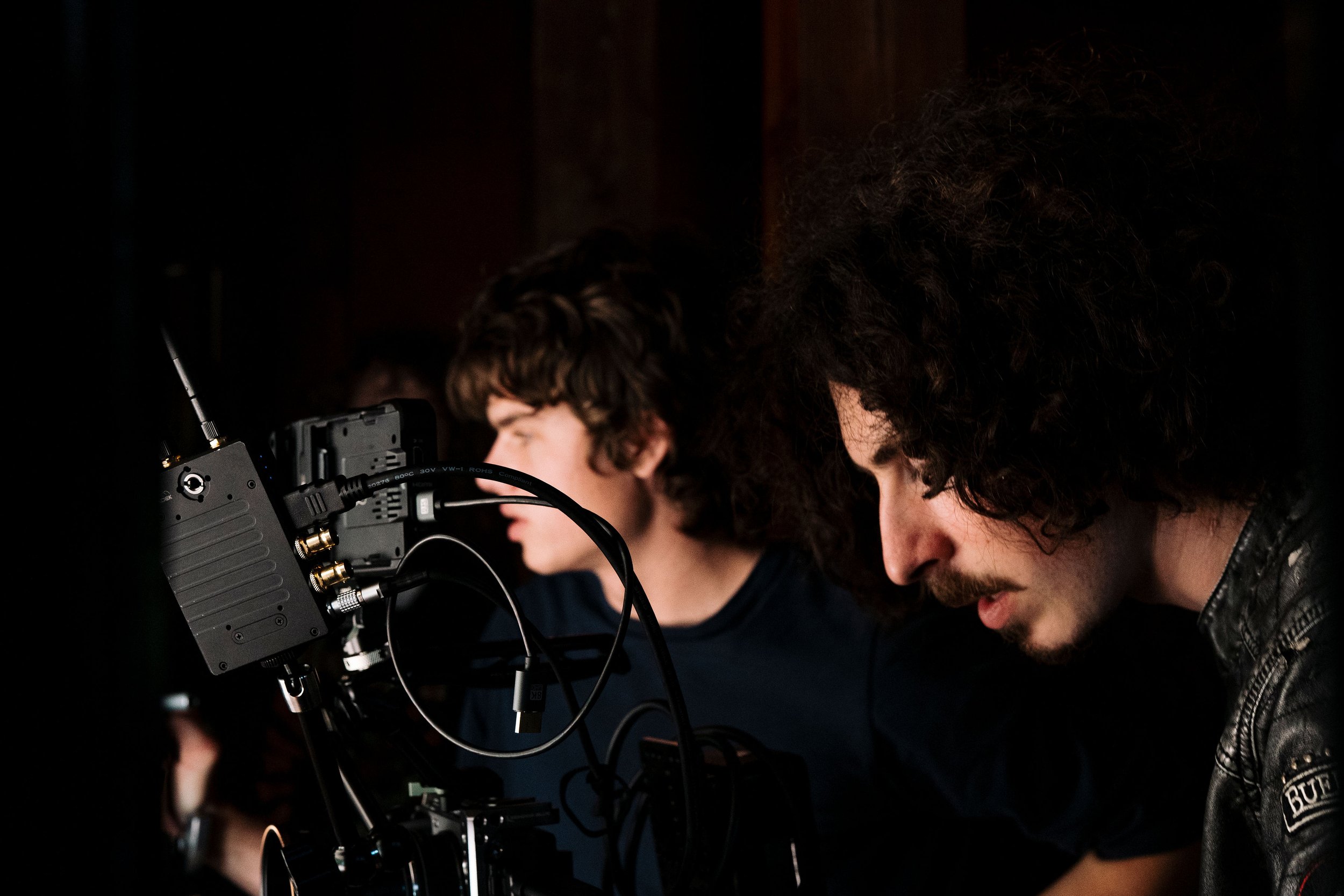 Two filmmakers operating a professional video camera in a dark production setting