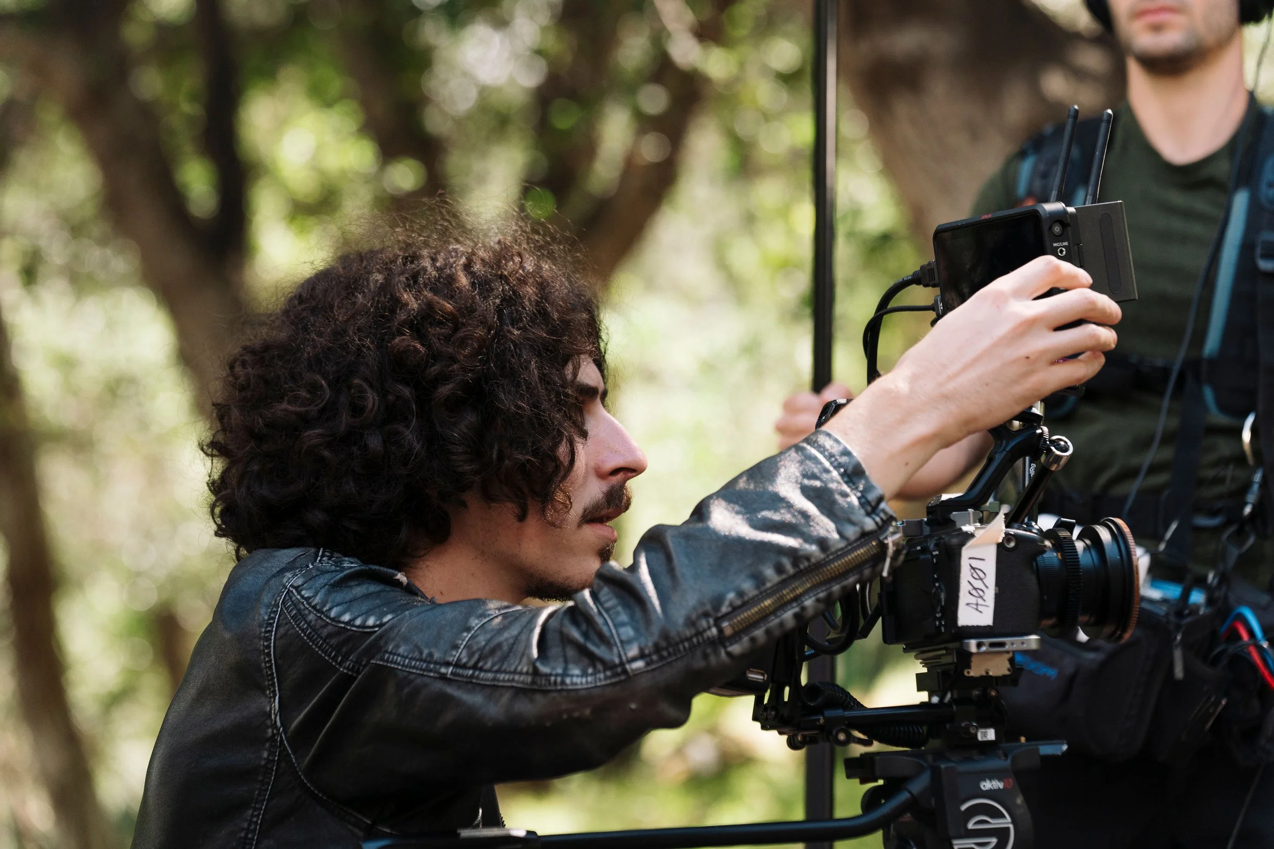 Filmmaker adjusting a professional video camera on a film set in a wooded outdoor location