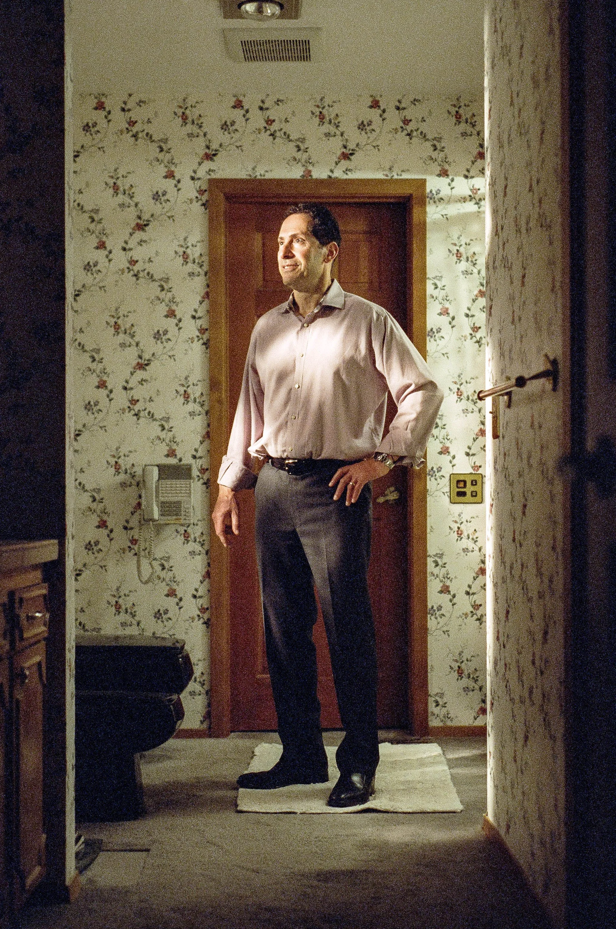 Man in a button-down shirt standing in a doorway of a vintage floral-wallpapered home