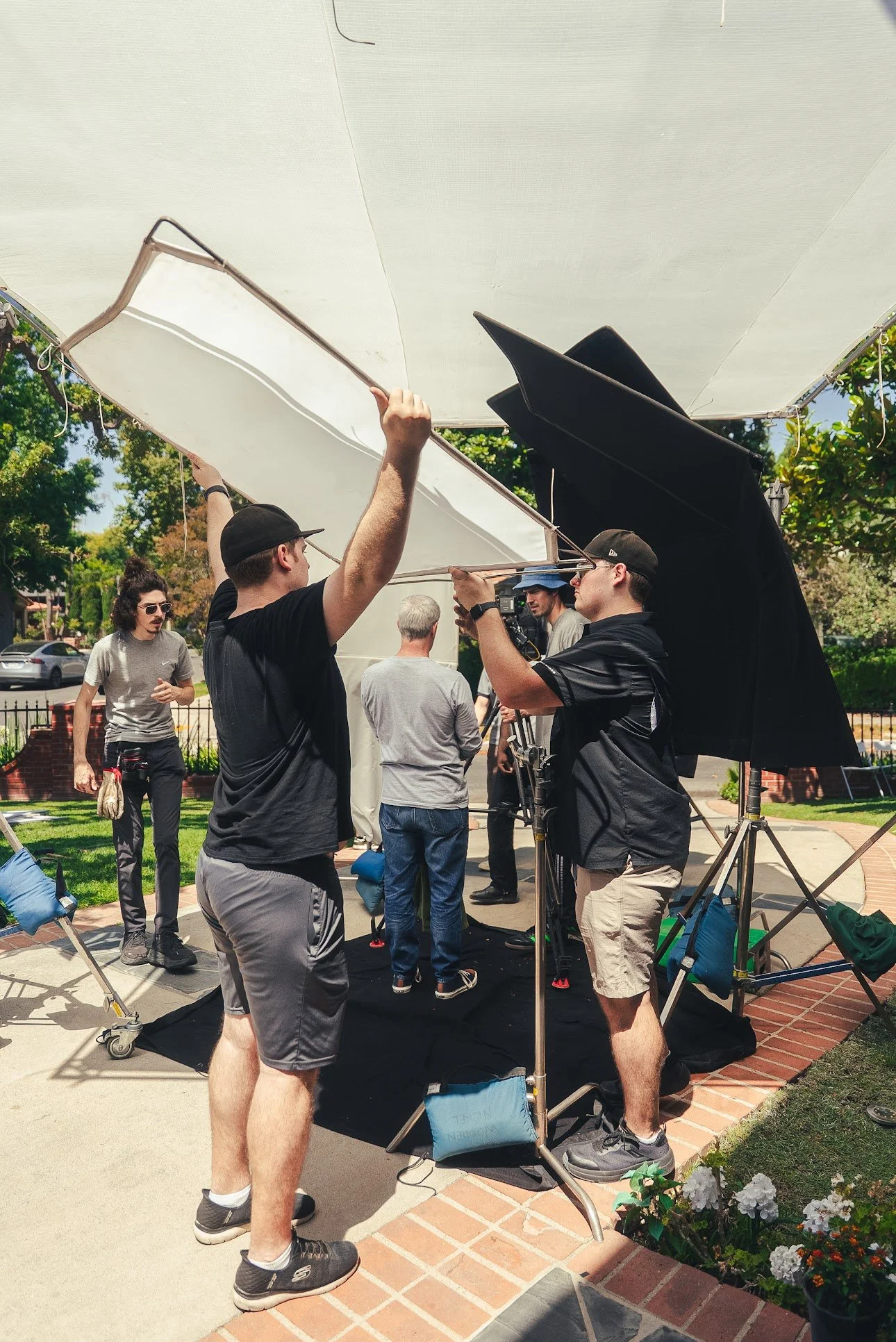 Film crew filming outdoors with large white and black reflectors, camera equipment, and lighting stands.