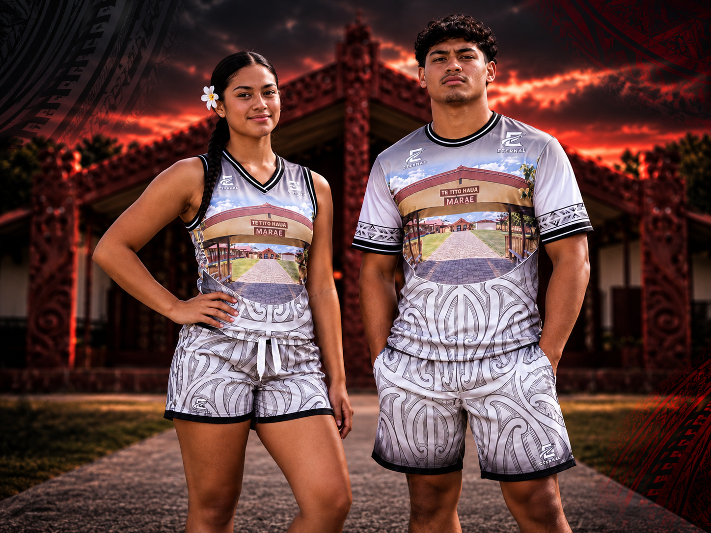 Two young people in matching traditional patterned athletic shirts and shorts standing outdoors in front of a red ornate building at sunset.