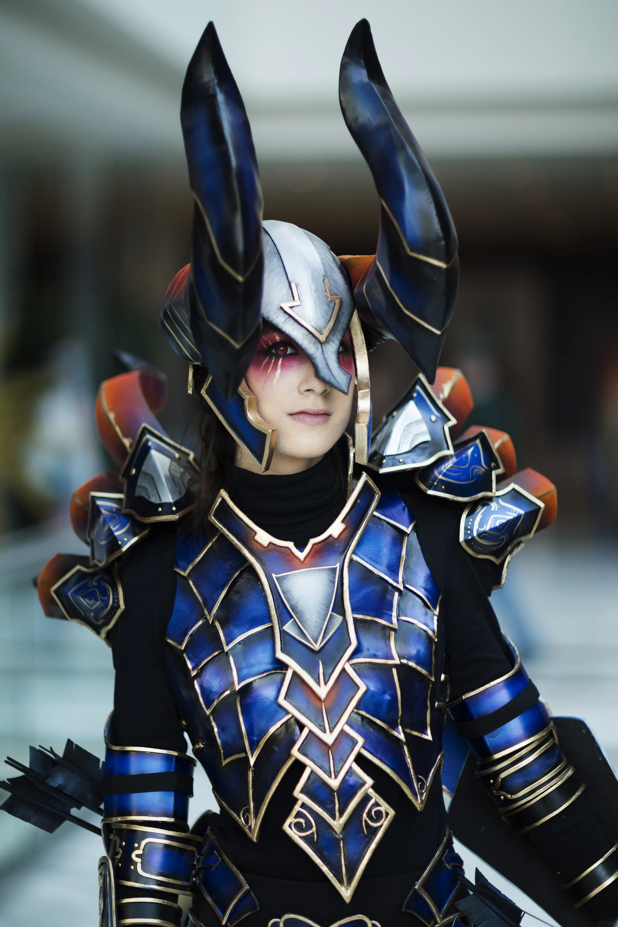 A person dressed in intricate fantasy armor with blue, black, and gold details and large horned headgear.