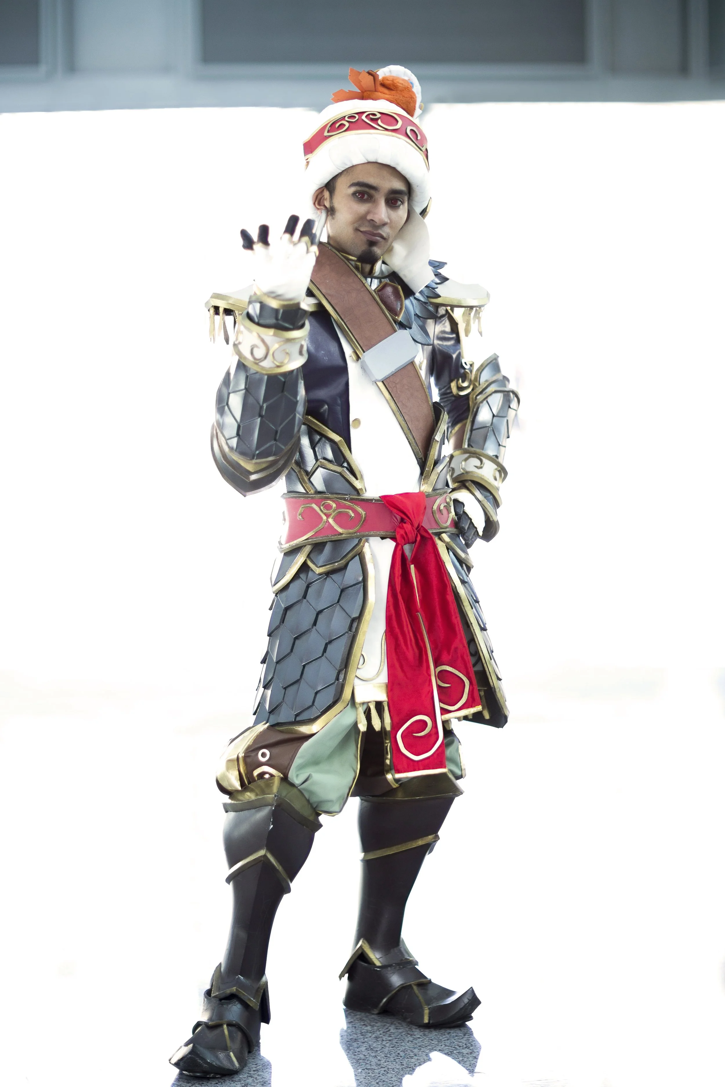 A person dressed in a detailed costume resembling a fantasy or gaming character, with armor, a colorful headpiece, and waving gesture.