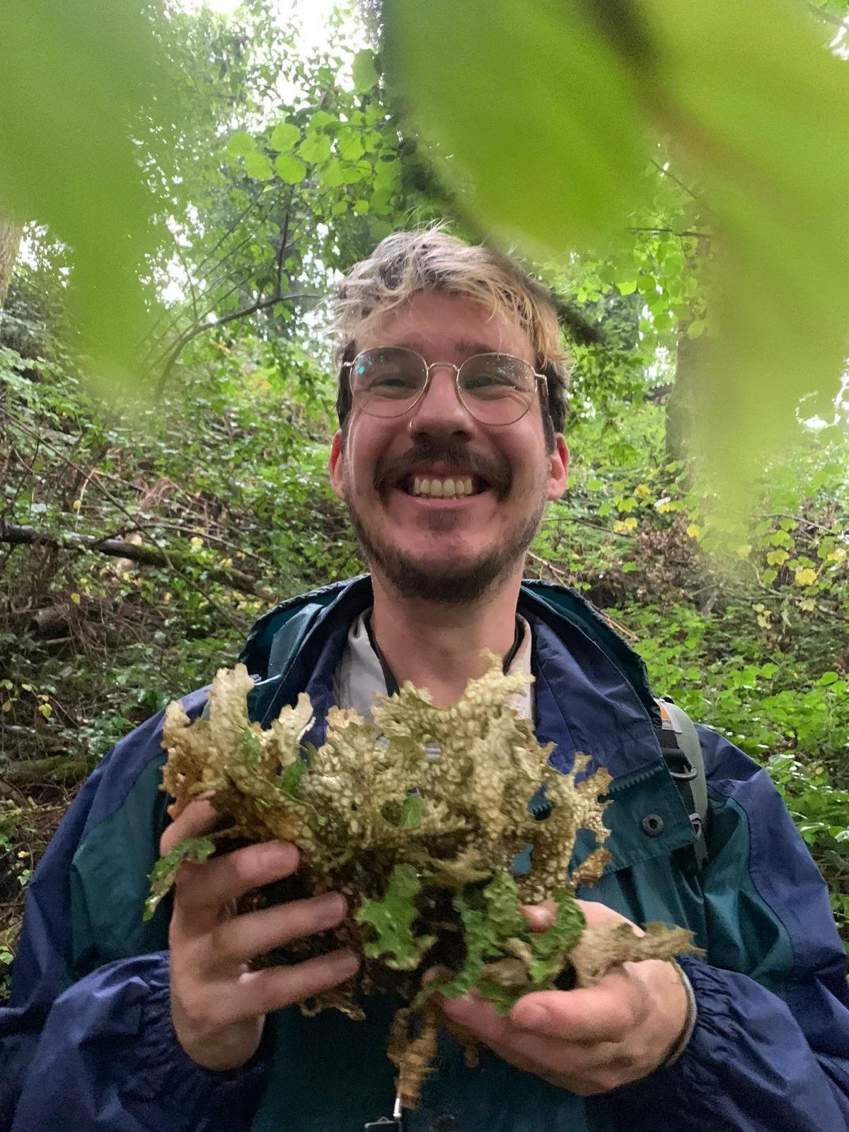 Jesse smiling in woodland, holding a bunch of foraged plants