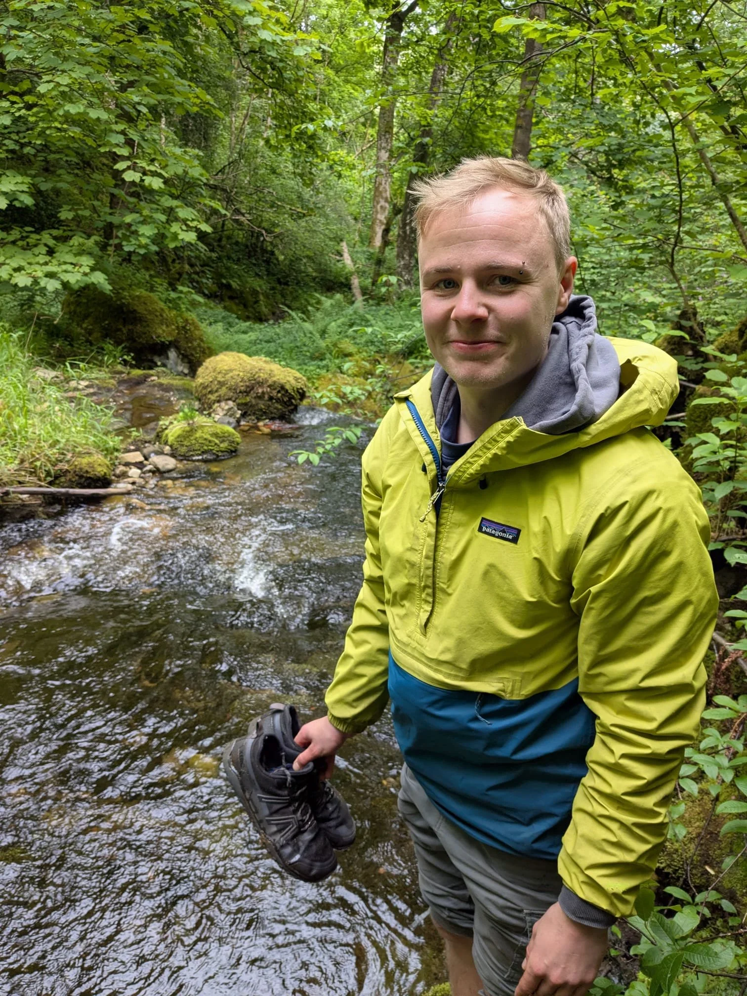 Rob standing in a woodland stream in a yellow and blue waterproof jacket