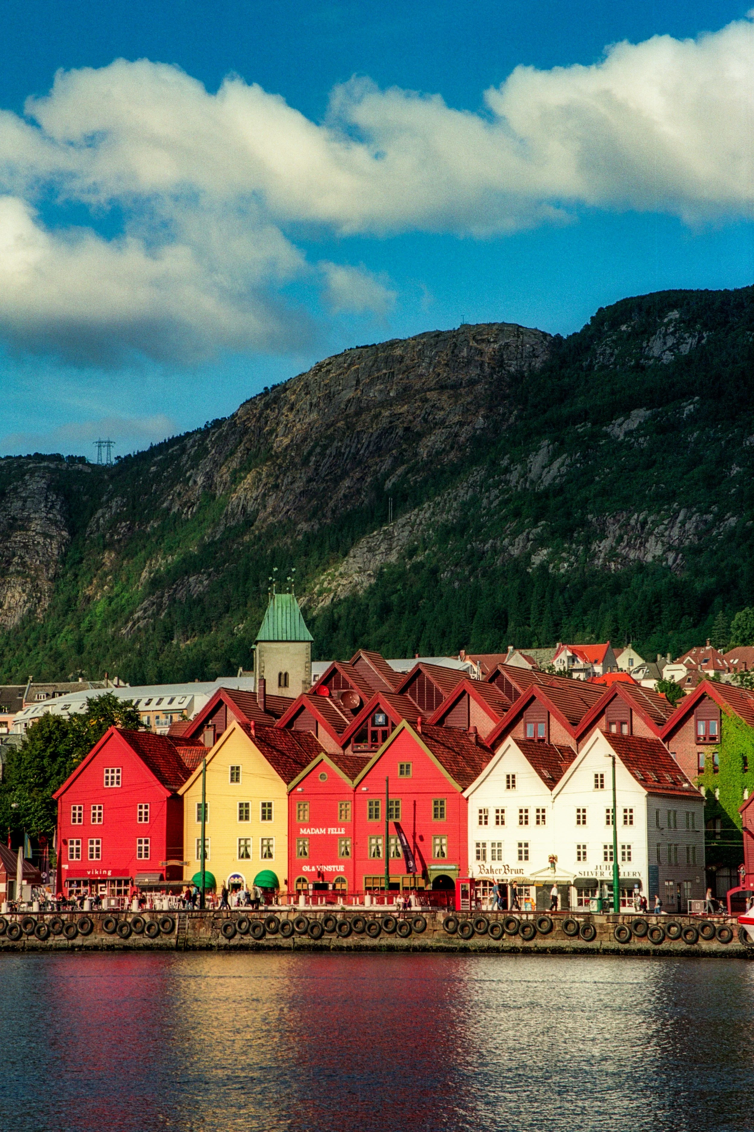Colorful houses along a waterfront with mountains and cloudy sky in the background.